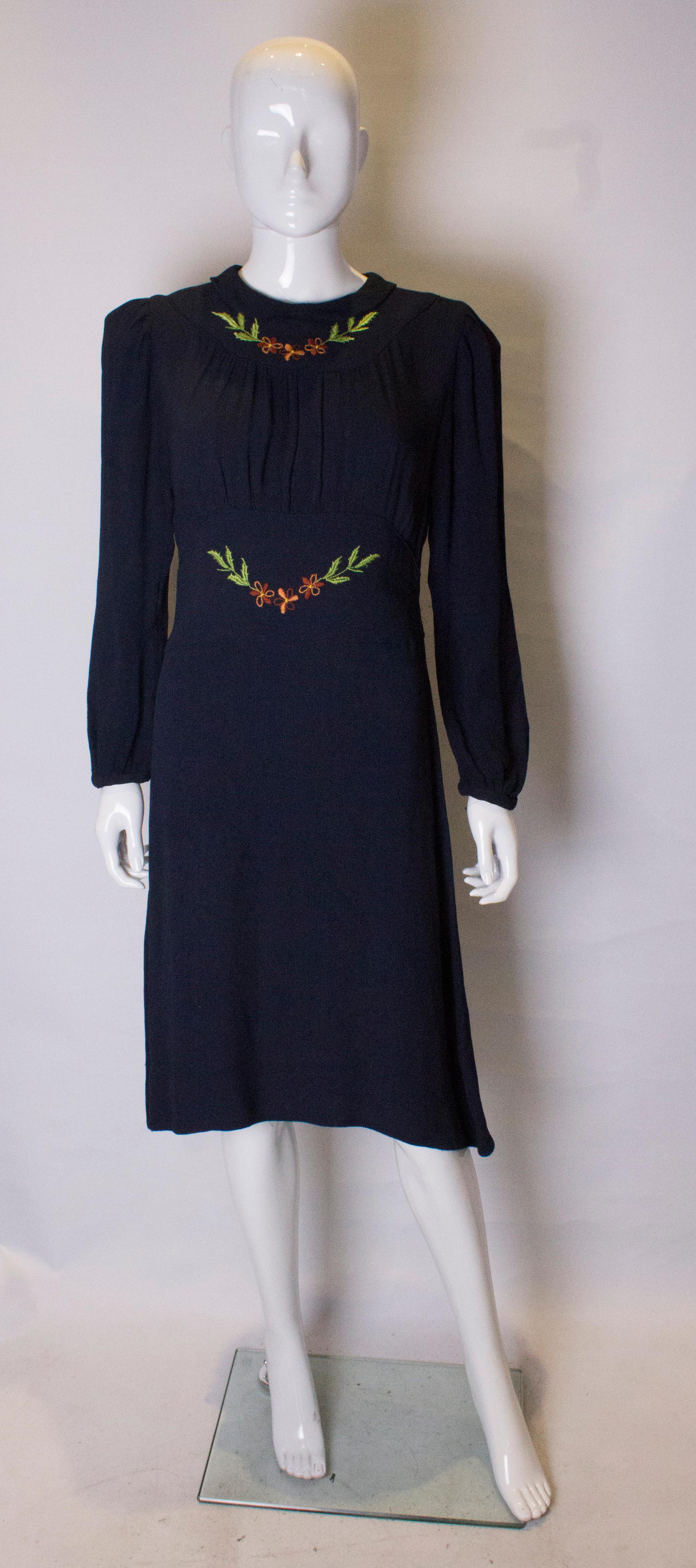 A pretty blue crepe dress with embroidery detail on the bust area and waist. The fabric is a pretty blue colour with a  subtle ribbed detail. It has a button opening at the back , and gathered sleeves with popper fastening.