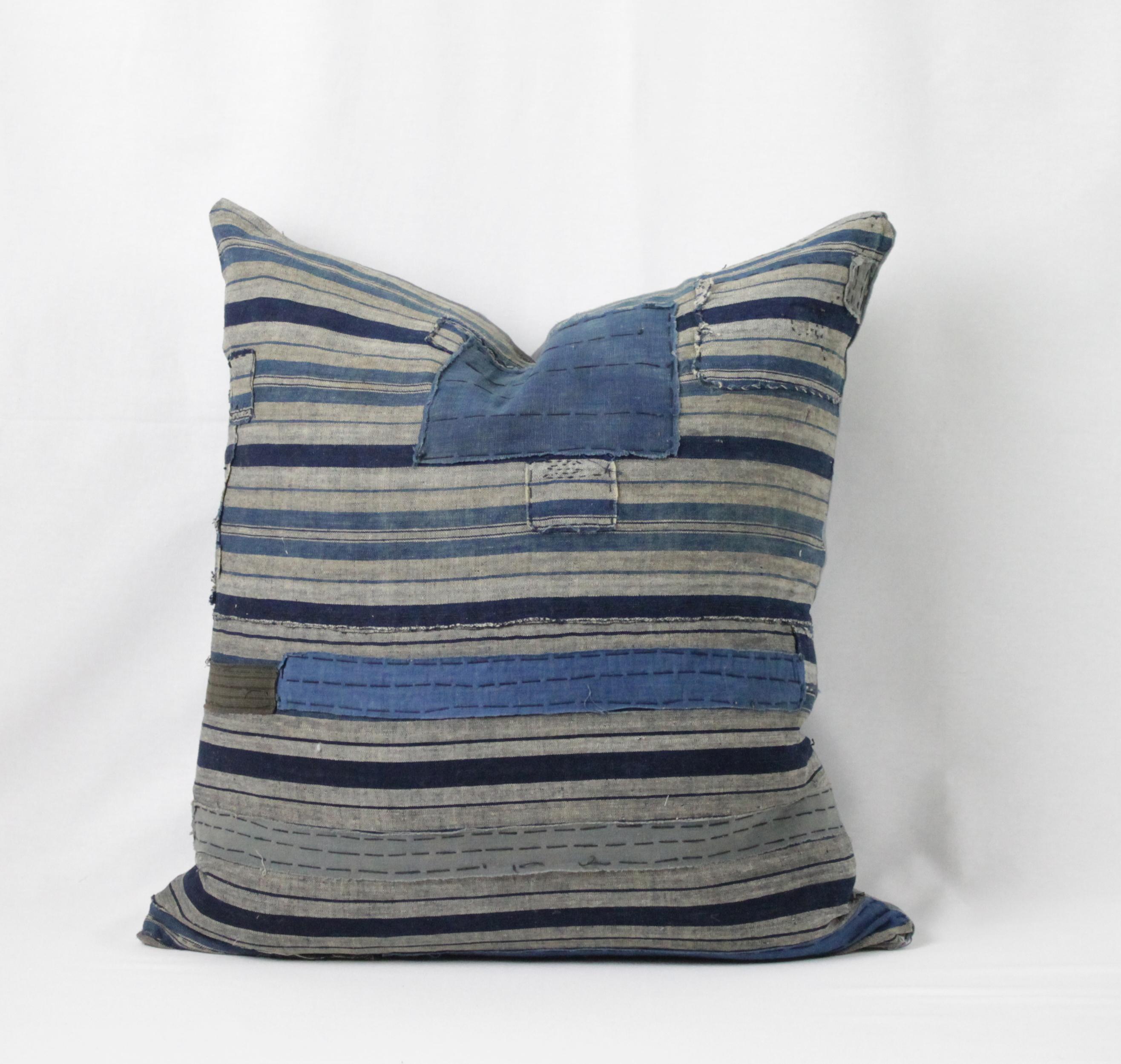 Blue patchwork horizontal style pillow, with zipper closure. Back is in grey linen. Main colors are medium blue, indigo blue, light blue color, tan, with black thread running through the design. Does not include insert. Measures 22