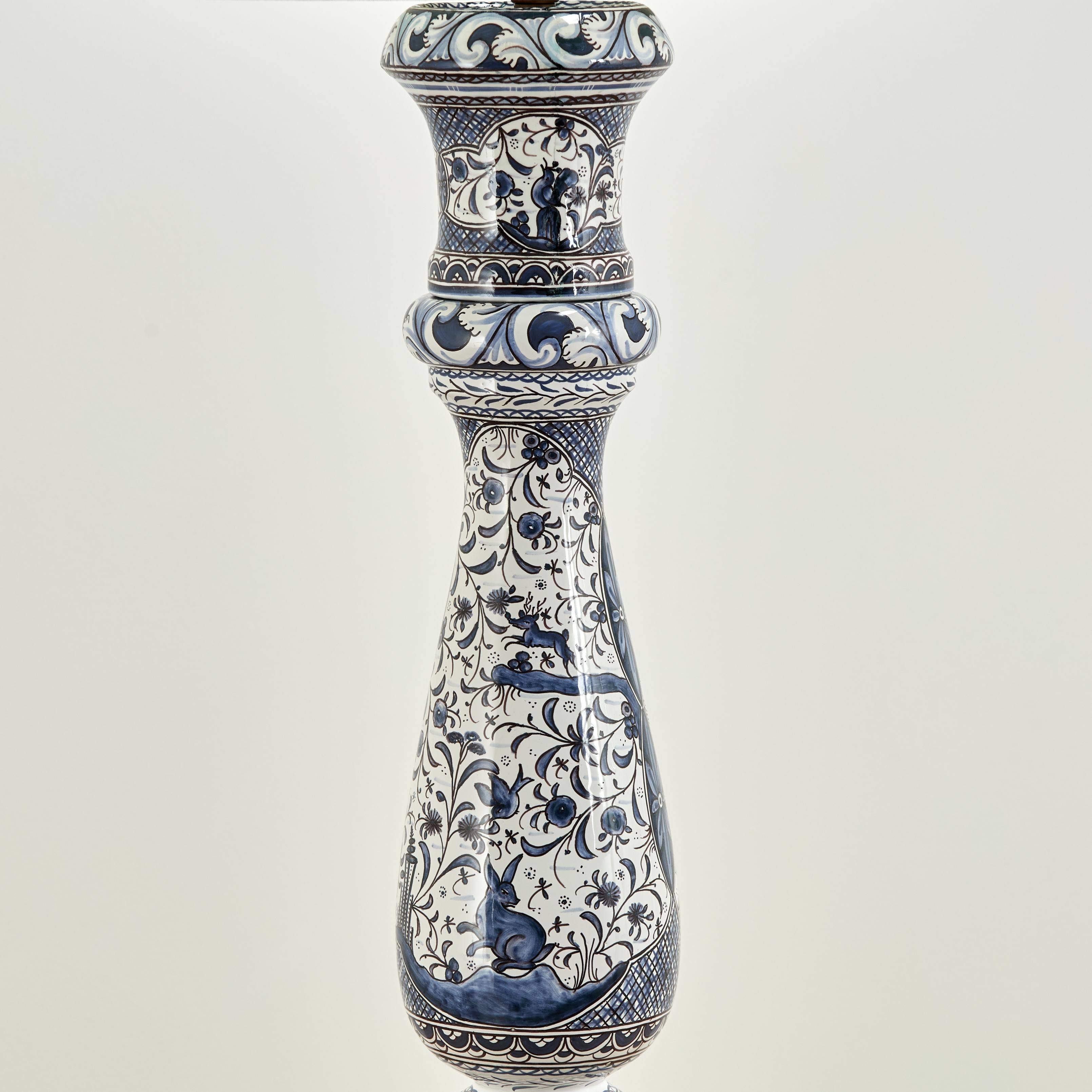 Lampada da terra vintage di grande effetto, realizzata in ceramica in forma classica e decorata a mano in un'affascinante composizione blu e bianca con conigli, uccelli, fiori e foglie d'acanto su una base in legno.