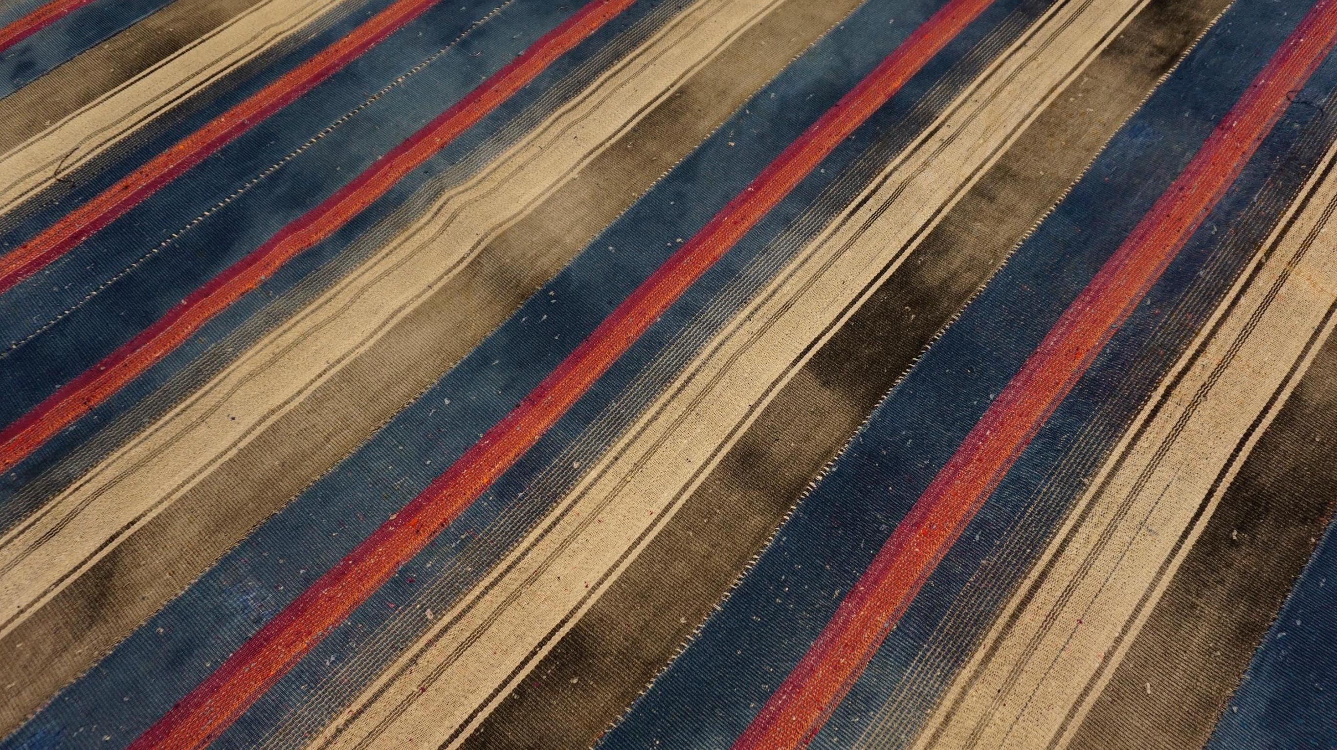 This vintage wool kilim presents a striking pattern of bold vertical stripes in vibrant hues of blue, beige, gray, exuding both a rustic charm and modern elegance. The contrasting colors and linear design offer a visually dynamic effect, making this