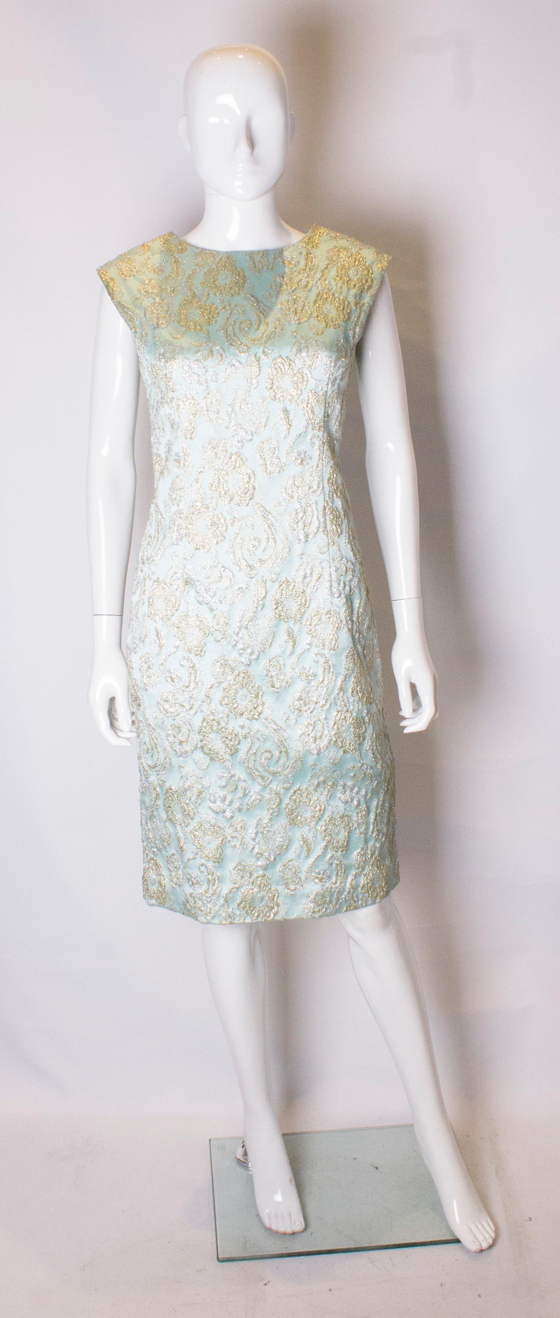 A pretty headturning cocktail dress. The dress is in a blue fabric with gold and silver embellishment. It has a  drape effect on the back and a central back zip. The dress is fully lined.