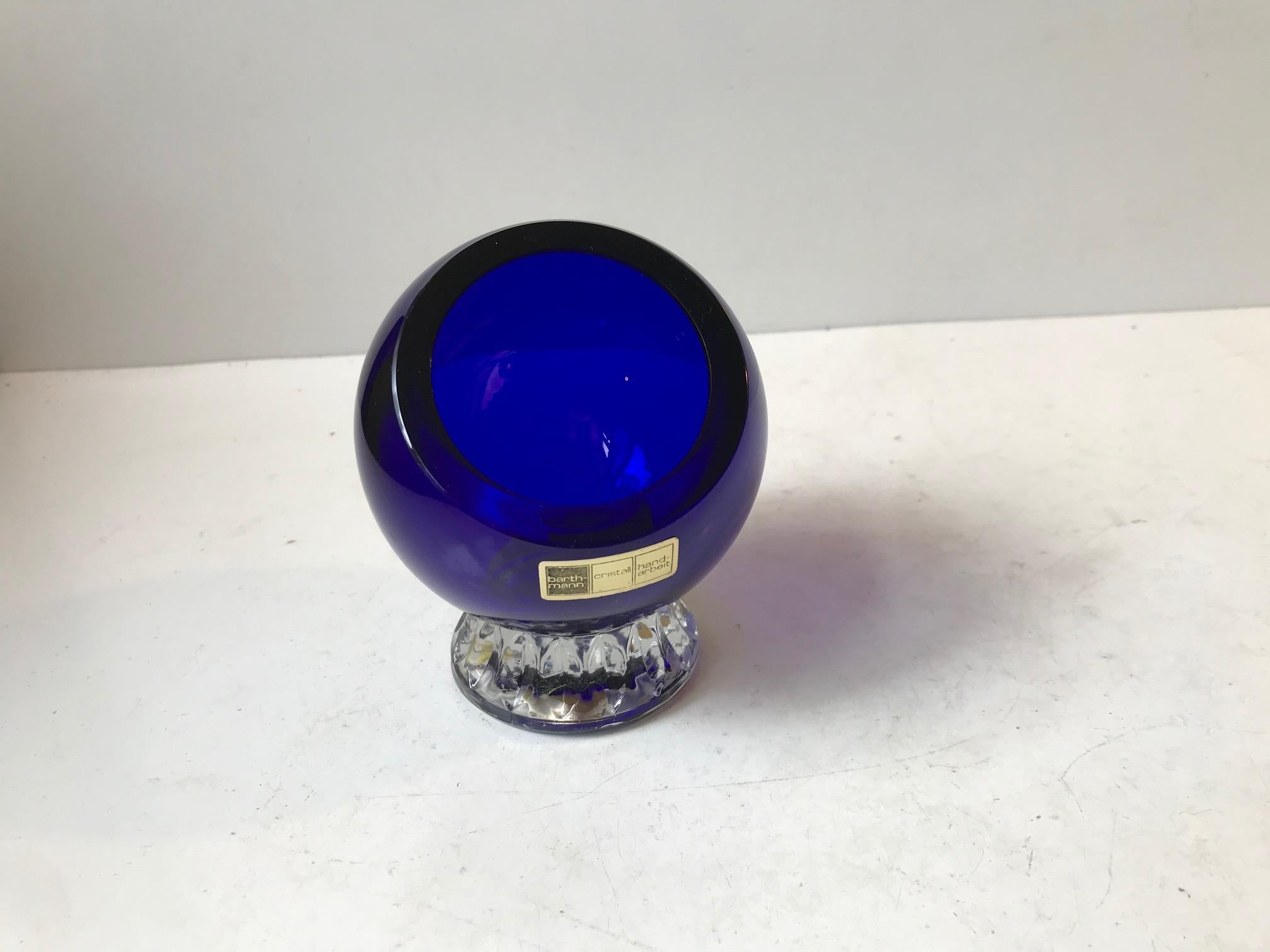 A small spherical footed ashtray in blue and clear handmade crystal. Designed and manufactured at Barthmann Glashütte in Germany circa 1970. It features maker mark and green table protecting filt to its underside. Measurements: H: 11, D: 8 cm.