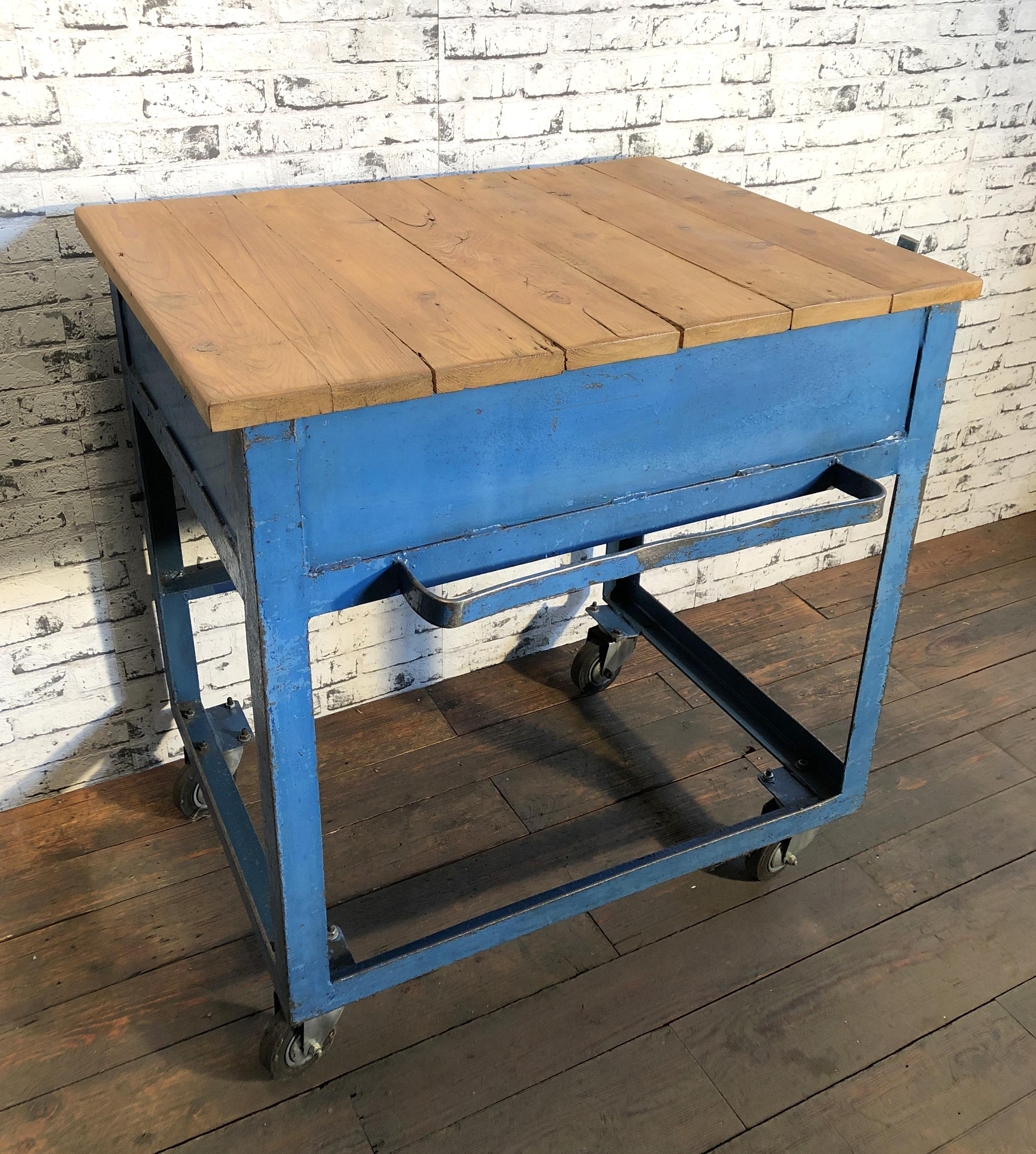 Vintage rolling table from 1950s. It features blue iron construction with four wheels and solid wooden plate.The top plate is hinged and the interior can be used. Weight : 50 kg.