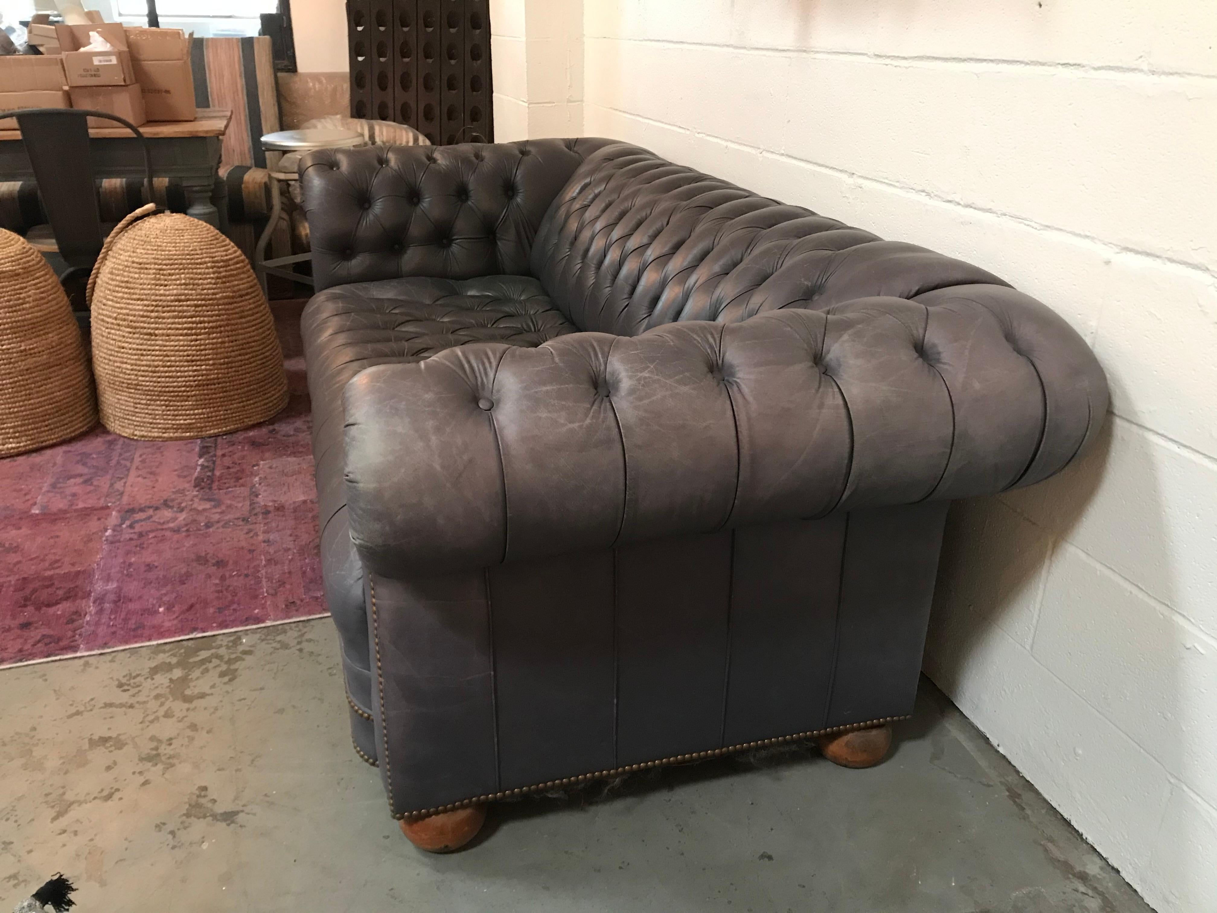 Vintage leather tufted sofa in a subtle blue hue. A wraparound seat design gives character to any room.