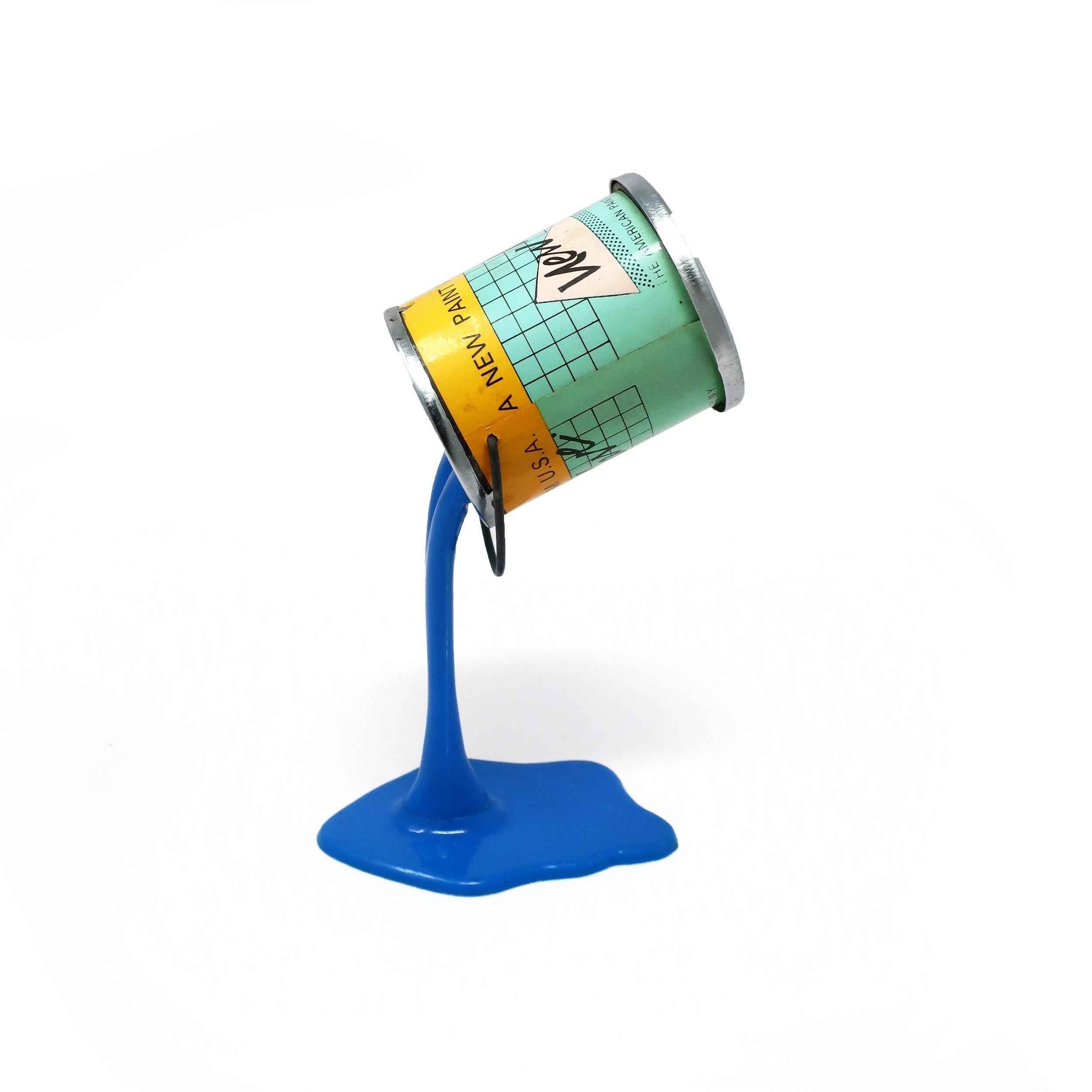 A perfectly Pop Art 1980s pouring paint can piggy bank/sculpture. Metal paint can with a quarter-sized coin slot in its bottom appears to be defying gravity by resting on a pouring stream of paint. Some people took the bottom off the paint can and