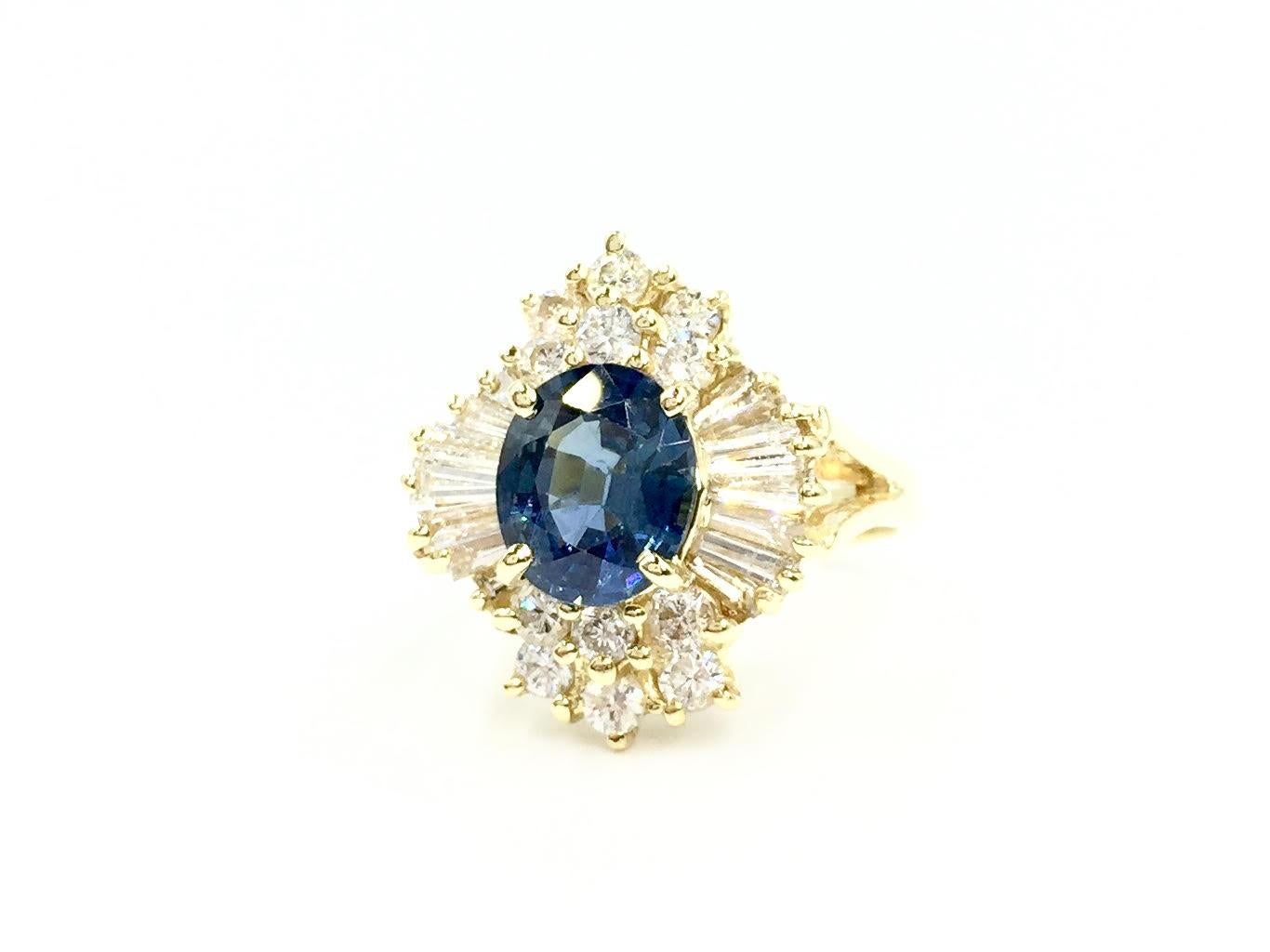 A gorgeous genuine medium blue oval sapphire is surrounded by baguette and round brilliant diamonds in this unique 18 karat yellow gold vintage Victorian inspired cocktail ring. Blue sapphire has a beautiful intense blueish-violet hue with