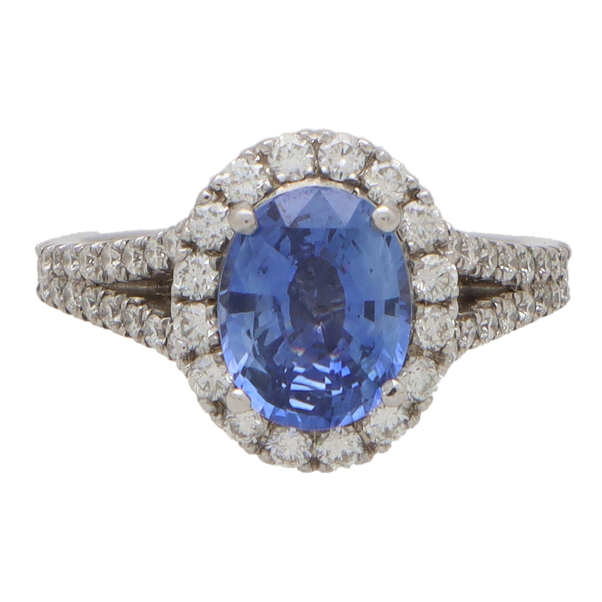 A beautiful bright blue sapphire and diamond oval halo ring set in 18k white gold.

The ring centrally features a beautiful blue coloured oval shaped sapphire surrounded by a halo of 16 round brilliant-cut diamonds. Each shoulder is split and micro