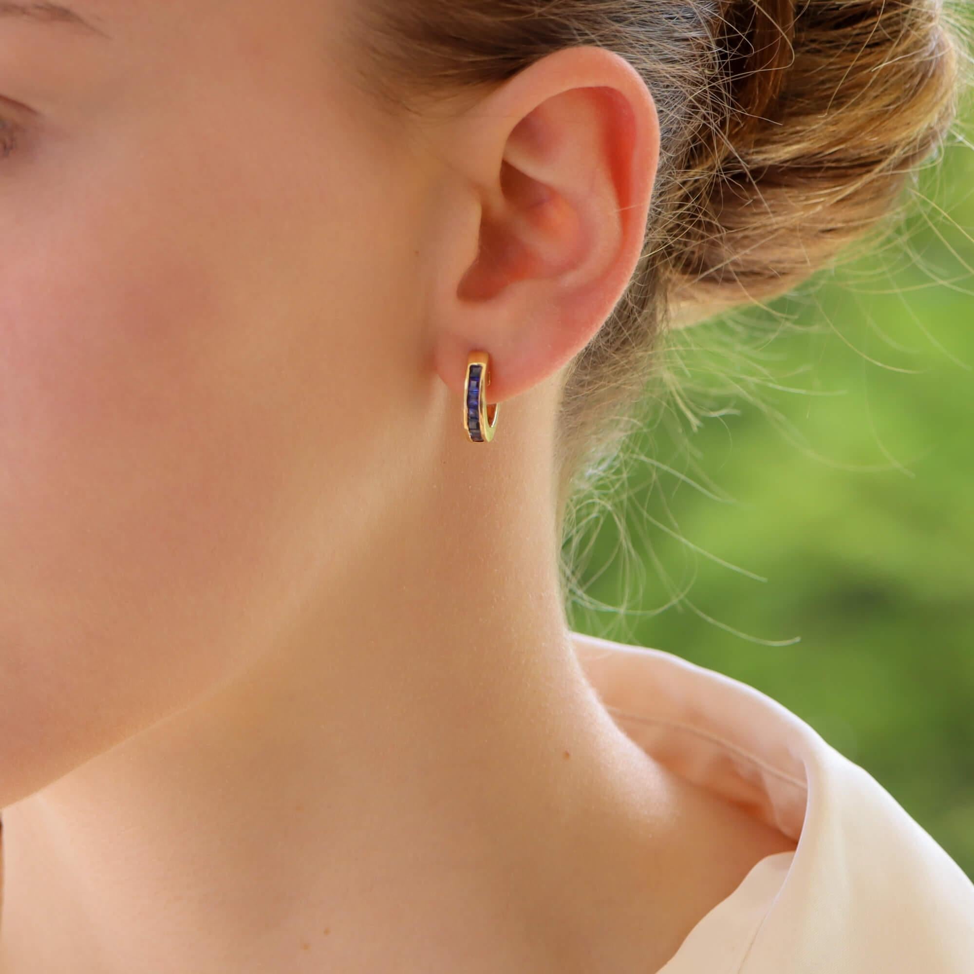  A stylish pair of vintage sapphire hoops set in 14k yellow gold.

Each earring is channel set with French cut blue sapphires which travel around the front of the hoops. They are each secured with a post and hinge shut fitting.

Due to the design