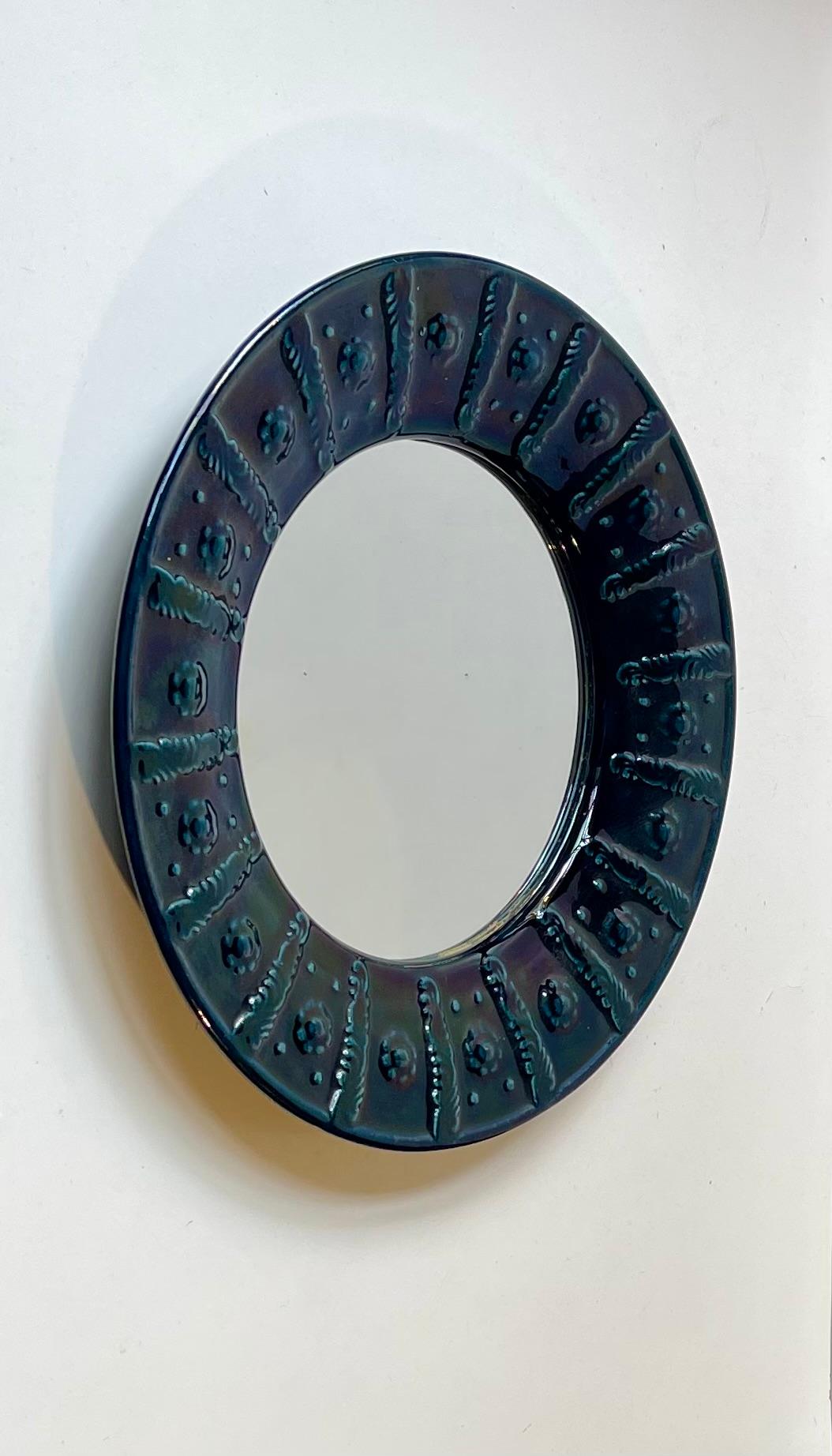 Miroir mural en céramique de taille convenable, mesurant 33 cm de diamètre. Il est exécuté dans une glaçure bleu sarcelle foncé couvrant des fleurs stylisées sur le pourtour. Fabricant scandinave inconnu vers 1970-80 dans un style rappelant