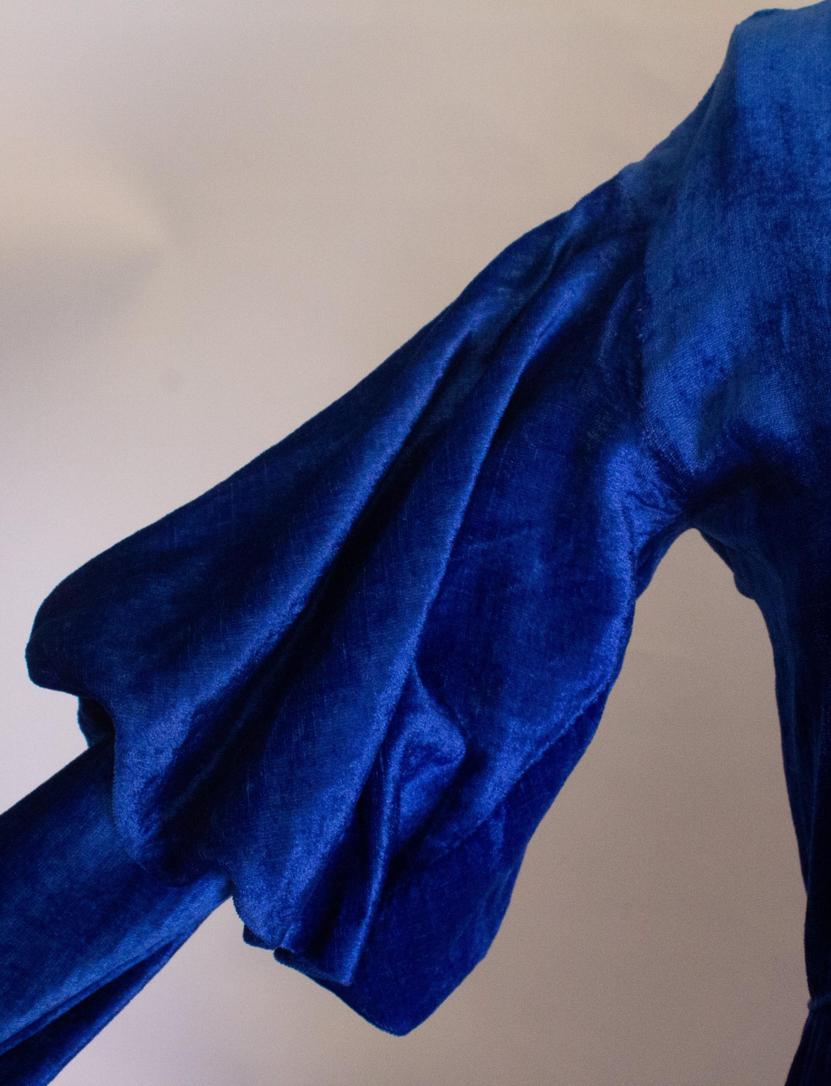 Une merveilleuse robe vintage dans un velours de soie bleu vibrant.  La robe a une encolure en V, des fermetures à boutons-pression et des manches en forme de bûche de mouton. Il a des poignets étroits qui pourraient  être ouvert.