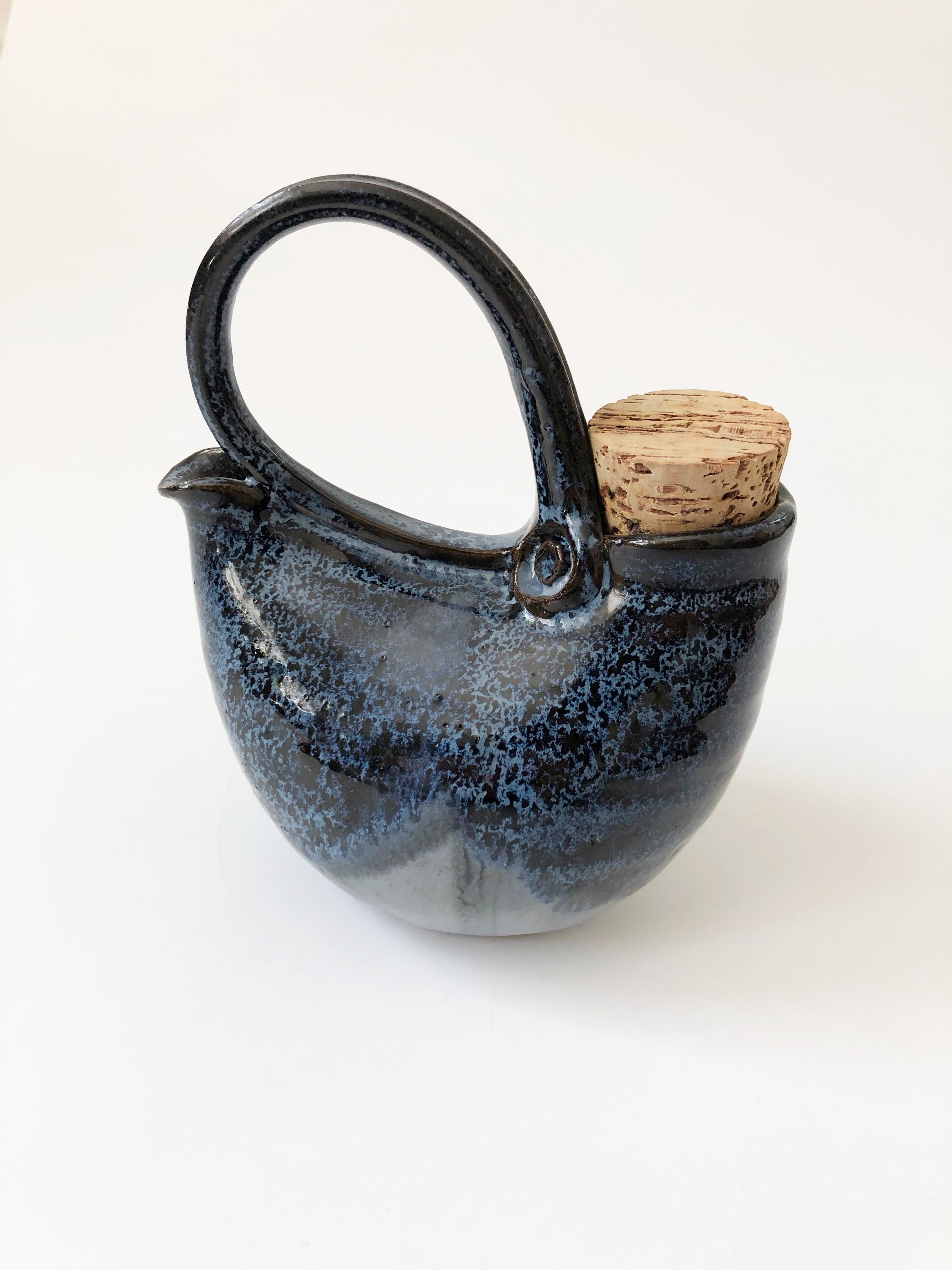A vintage studio pottery teapot in a great unique handmade shape. Features a large curved handle that leads from spout to the filling hole that is plugged by a cork. Nice round shape, finished in an earthy two toned blue glaze. A great sculptural