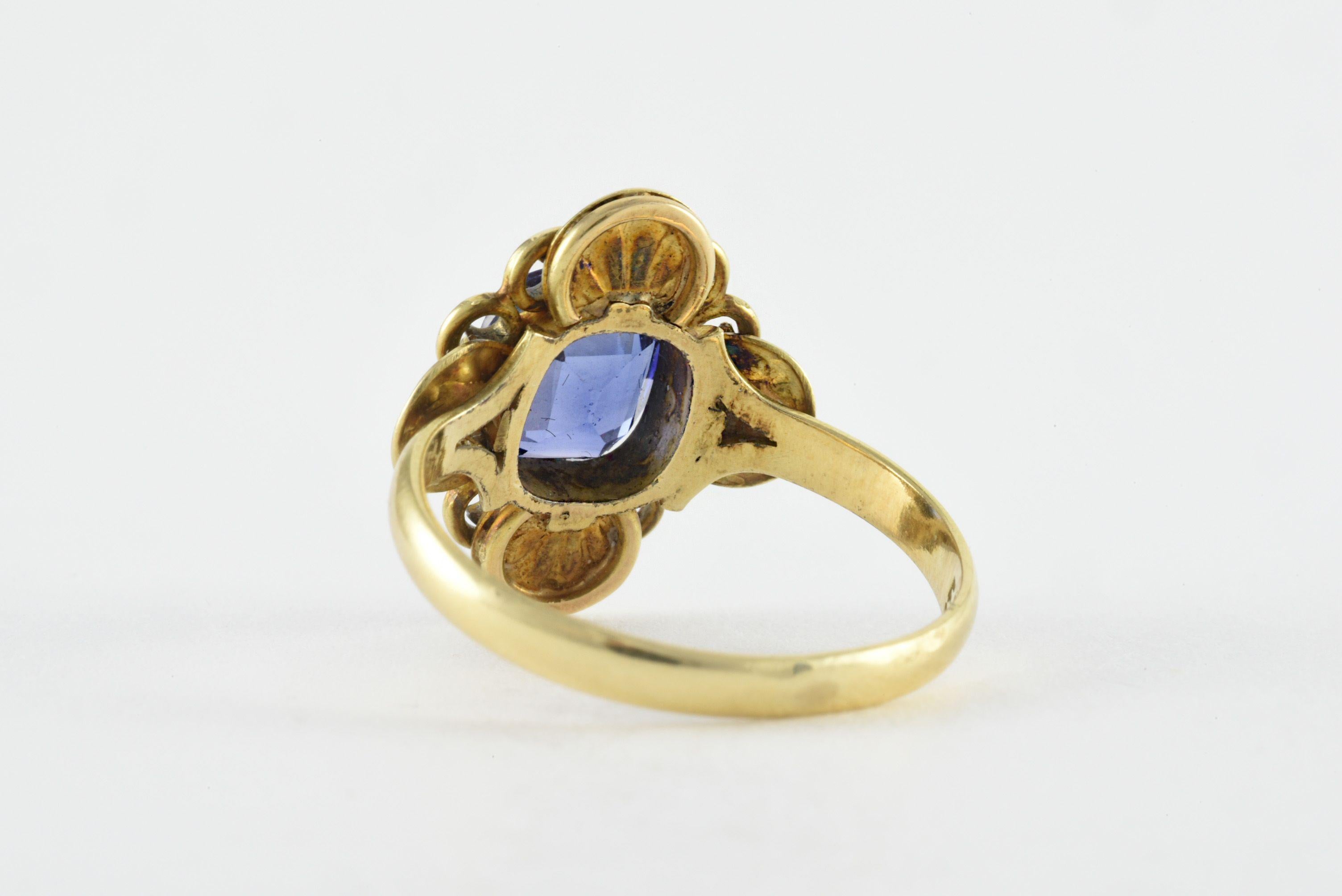 A vibrant blue cushion-cut synthetic sapphire measuring 6.4 x 7.5 x 3.8mm centers this vintage band fashioned from 14kt yellow gold surrounded by a swirling floral design. Stamped 
