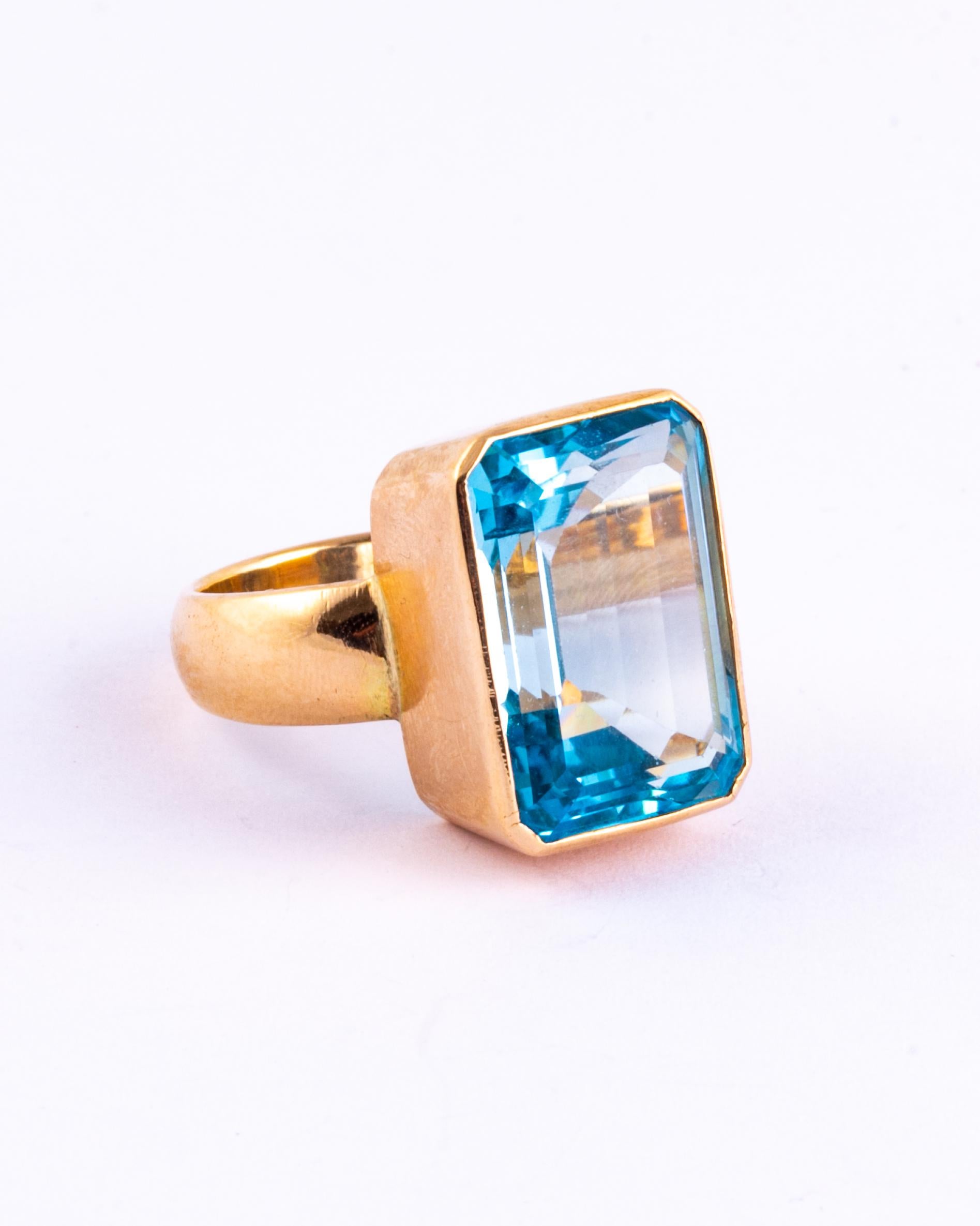 What a show stopper! The bright blue topaz is emerald cut and reflects the light beautifully and shows off the colour of the stone. The extra wide 9 carat gold band sweeps up and encases the stone and becomes the setting in which it sits.  

Ring