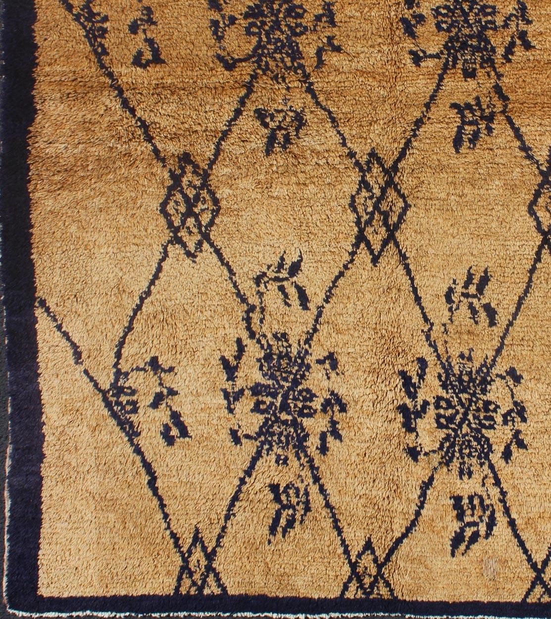 This unique Tulu demonstrates a balance between a tribal motif and a freely floating floral design. The navy pattern contrasts elegantly with the warm taupe background, encased by a solid, defined border. With its agrestic charm, plush pile and