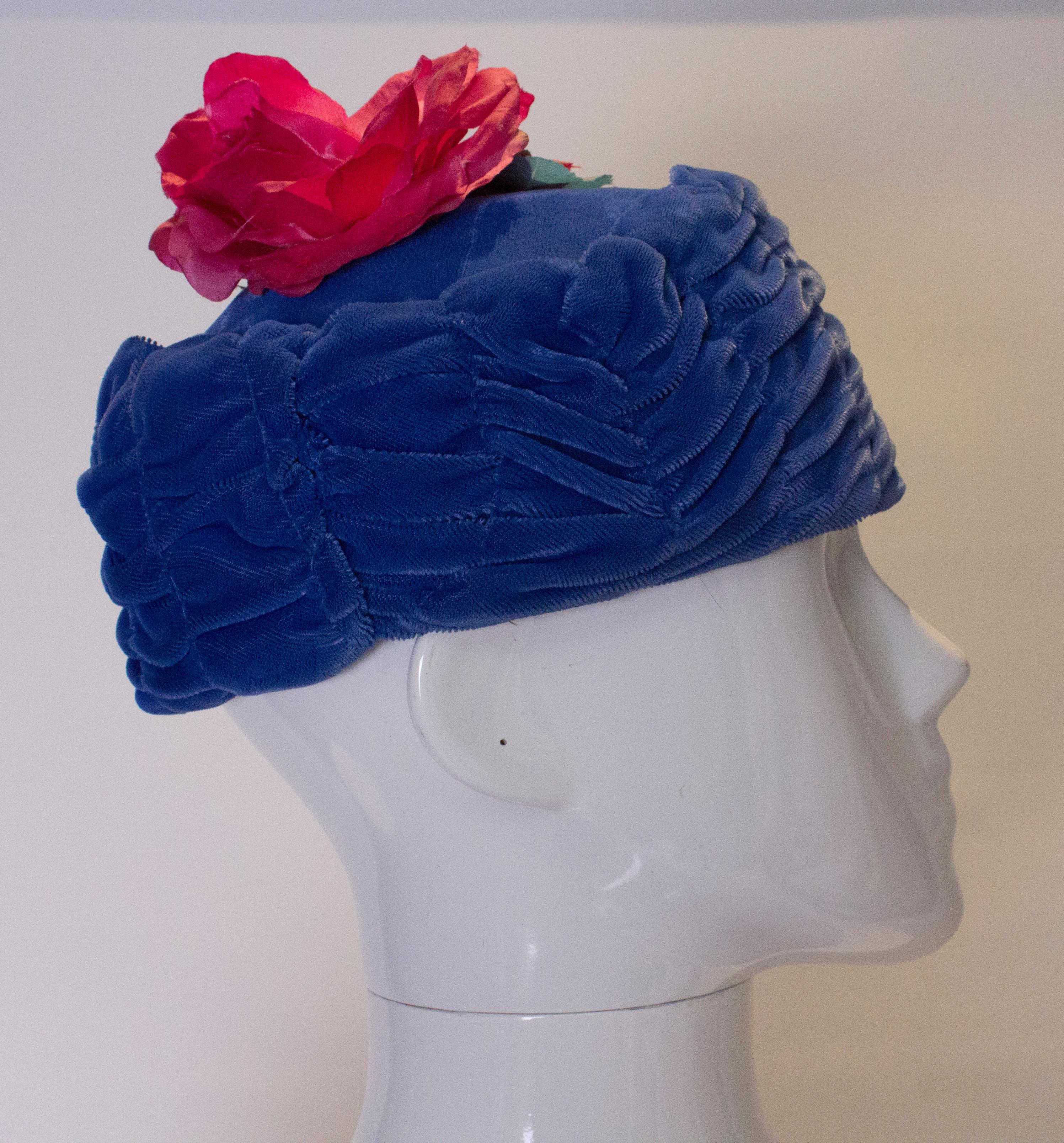 A chic blue velvet vintage hat , with a decorative pink flower on top. The hat is lined in net, and the inner circumference measures 22''.