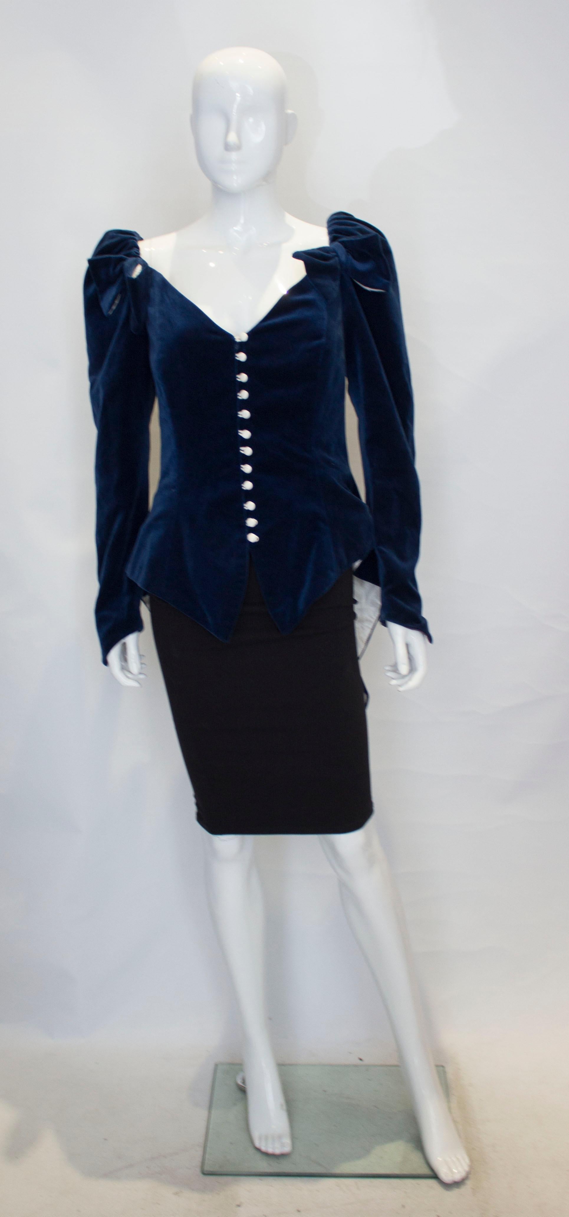 A head turning jacket in blue velvet by Renee Joyce, Princess Collection.  The jacket has elasticated shoulders and so can be worn , on or off the shoulder. It has a central white button fastening and cuffs with a velvet bow at the back. It is fully