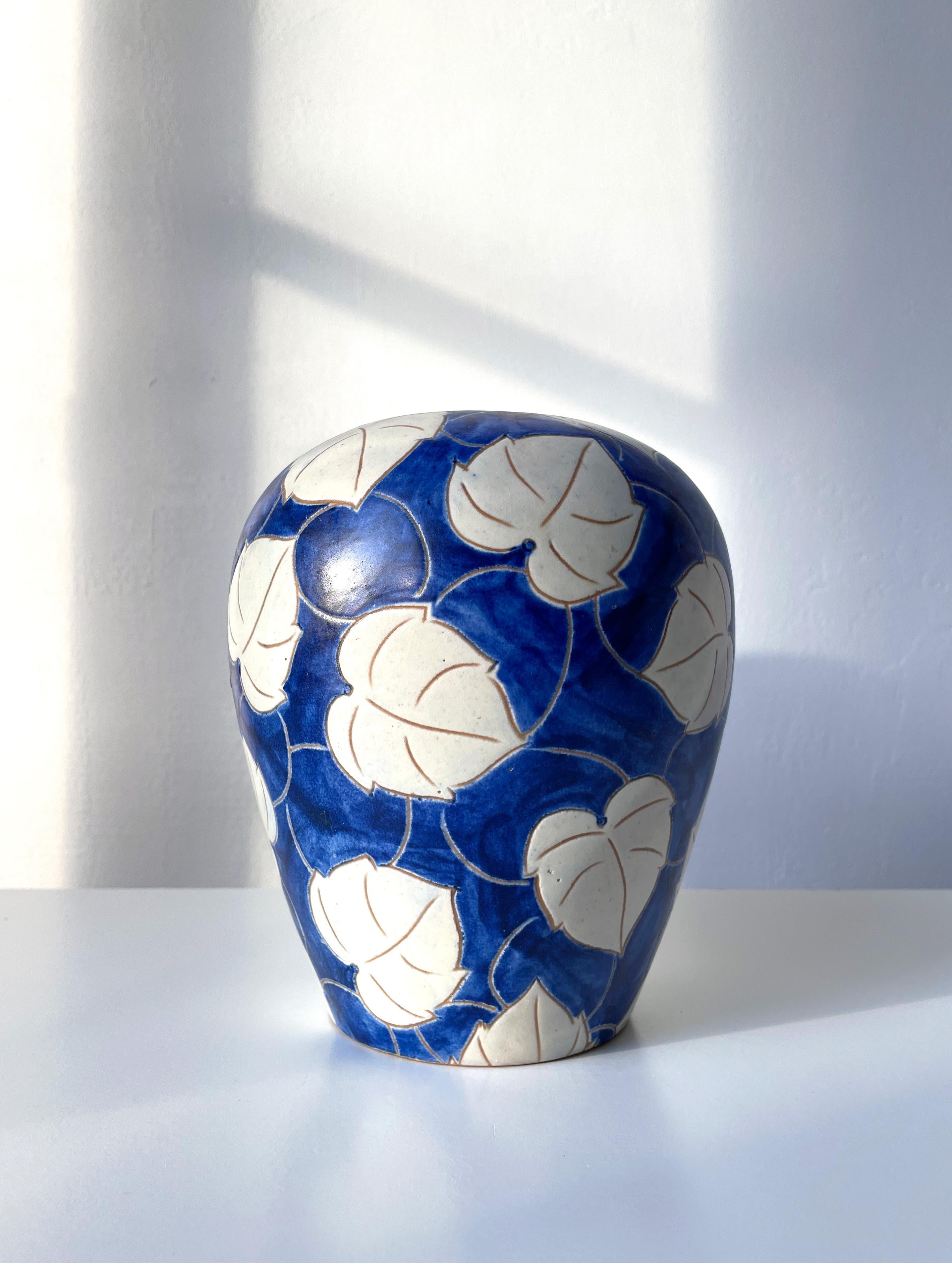 Weich geformte dänische Keramikvase aus den 1950er Jahren im organisch-modernen Art-déco-Stil von Eslau, handgefertigt. Handgeschnitzte, stilisierte weiße Blätter auf tiefblauem, handbemaltem Hintergrund. Unter dem Sockel signiert. Schöner