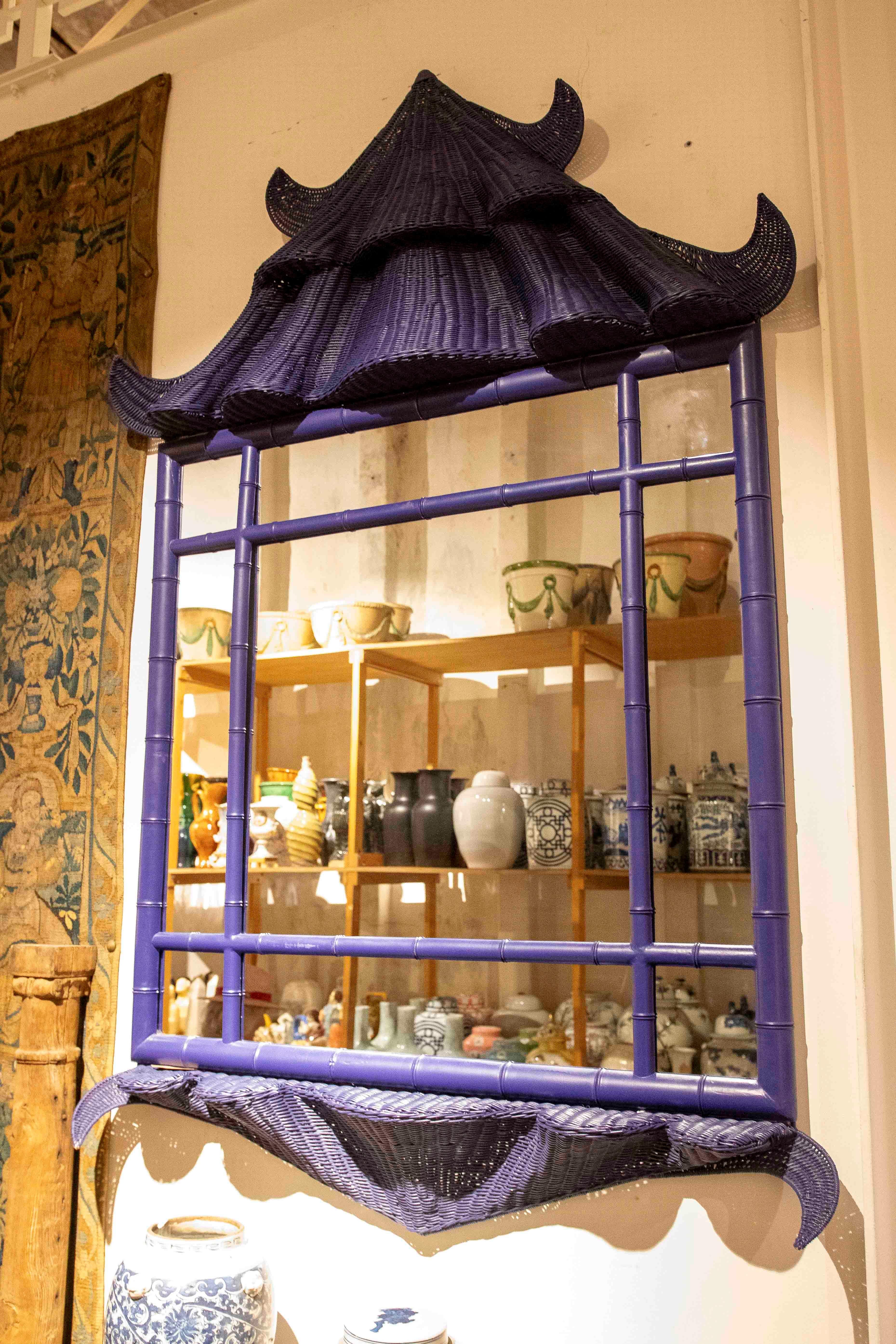 Un originale specchio decorativo vintage dipinto in una tonalità blu intenso, con una cornice in vimini che imita la silhouette di una pagoda asiatica. Il design intricato della struttura in bambù aggiunge un tocco esotico ed elegante, ideale per