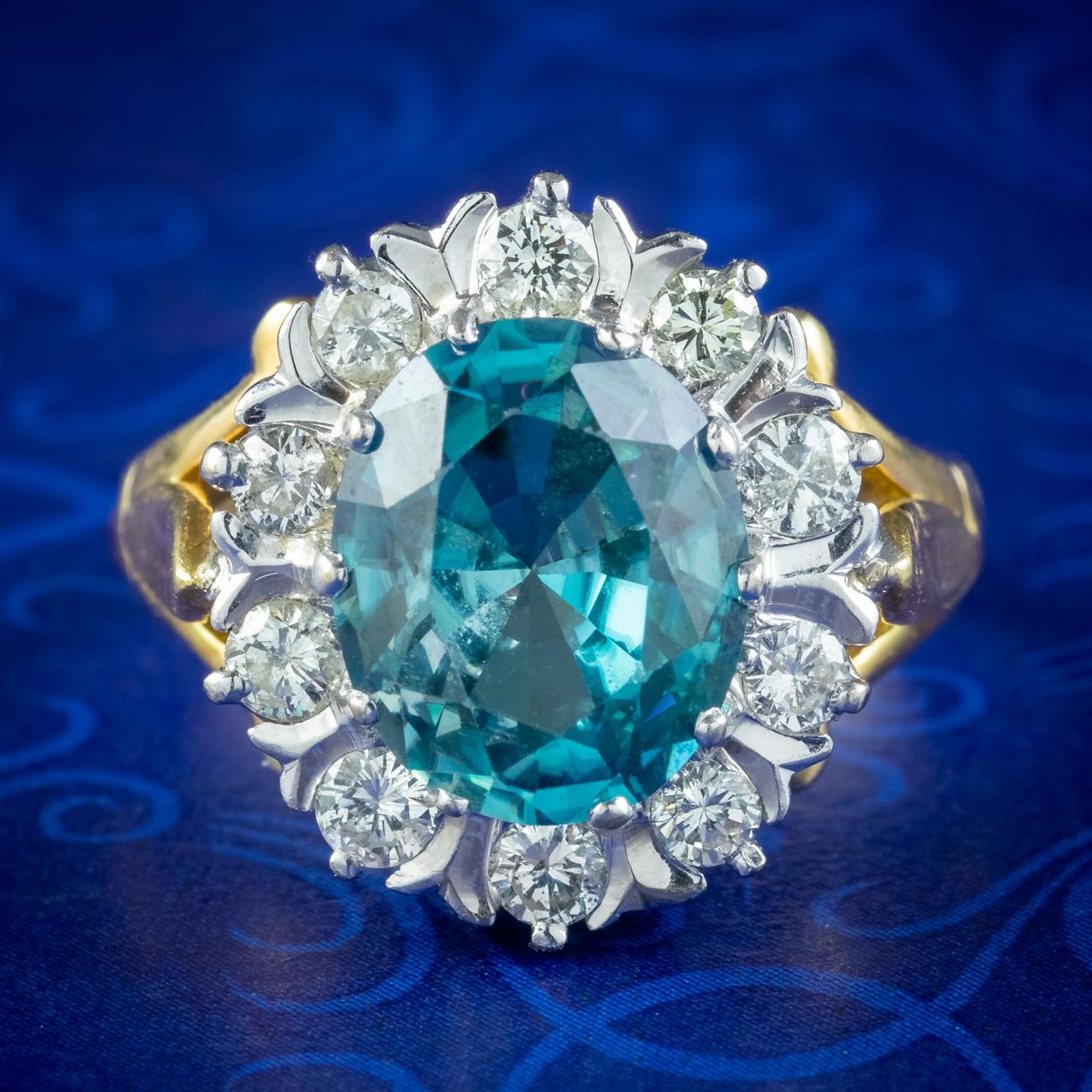 Ein spektakulärer Vintage-Cluster-Ring, gekrönt von einem funkelnden Zirkon im Ovalschliff mit tiefem blaugrünem Farbton. Er wiegt ca. 3 ct und wird von zehn funkelnden Diamanten im Brillantschliff umrahmt, die insgesamt ca. 0,80 ct