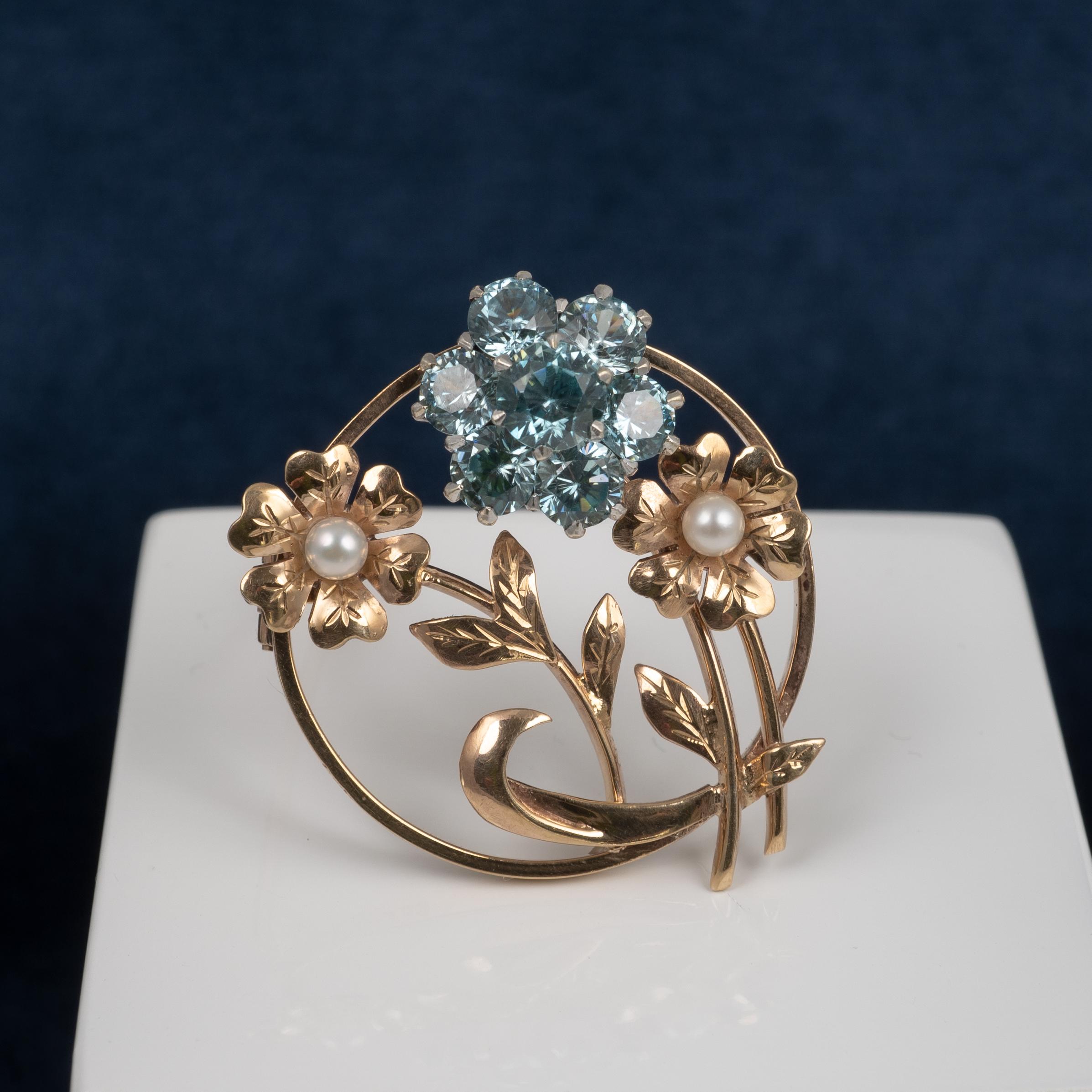 A vintage gold circular flowers brooch features 2.4-carat blue zircon flower cluster with 2 seed pearl accents.

The electric blue zircon flower cluster is complemented by two detailed gold flowers set with round cultured pearls. The curved brooch