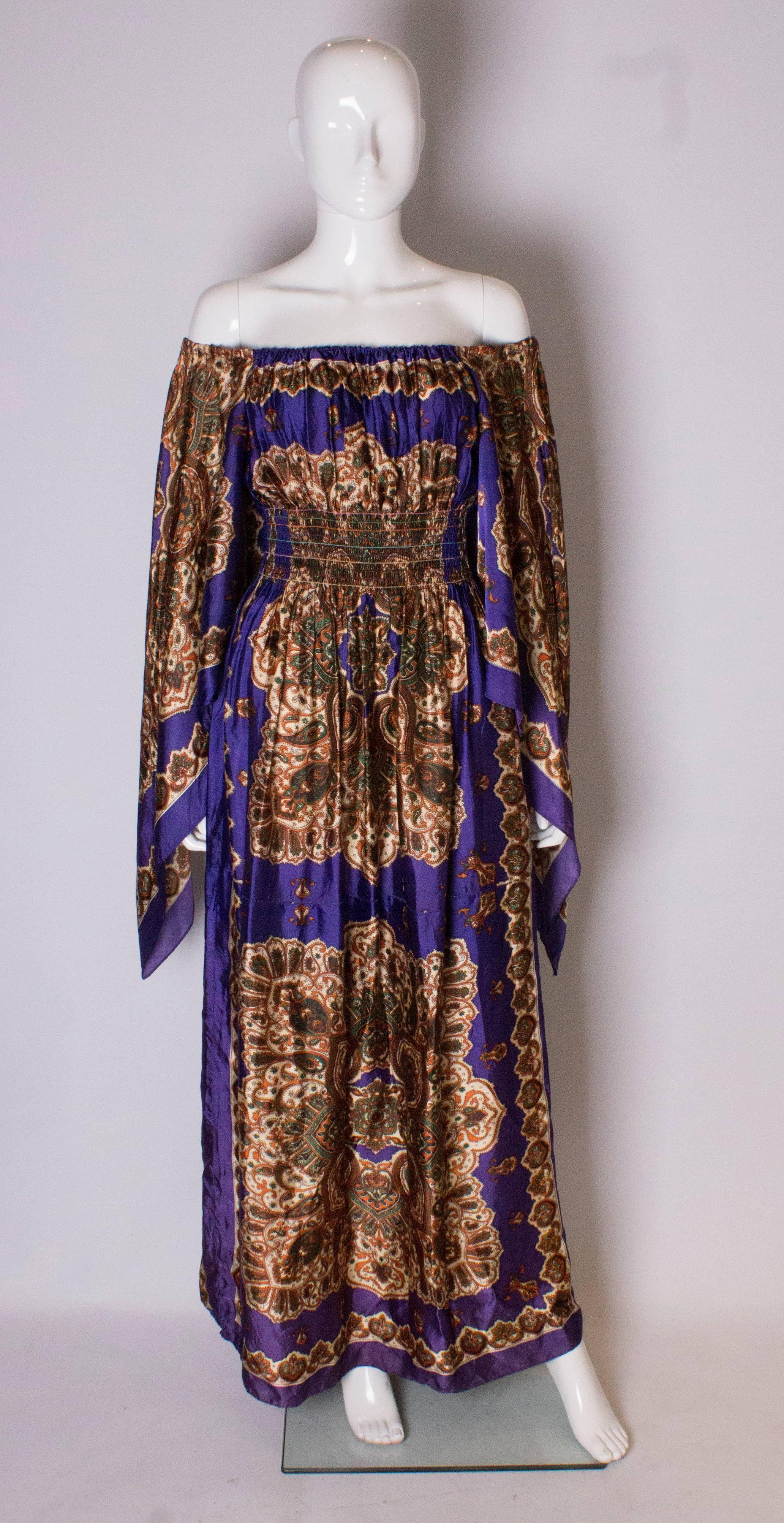 A great boho festival  dress from the 1970s. ,. The dress has an elastic neckline, hankerchief sleaves,  and an elastic waist.,It  is purple in colour with a paisley print.