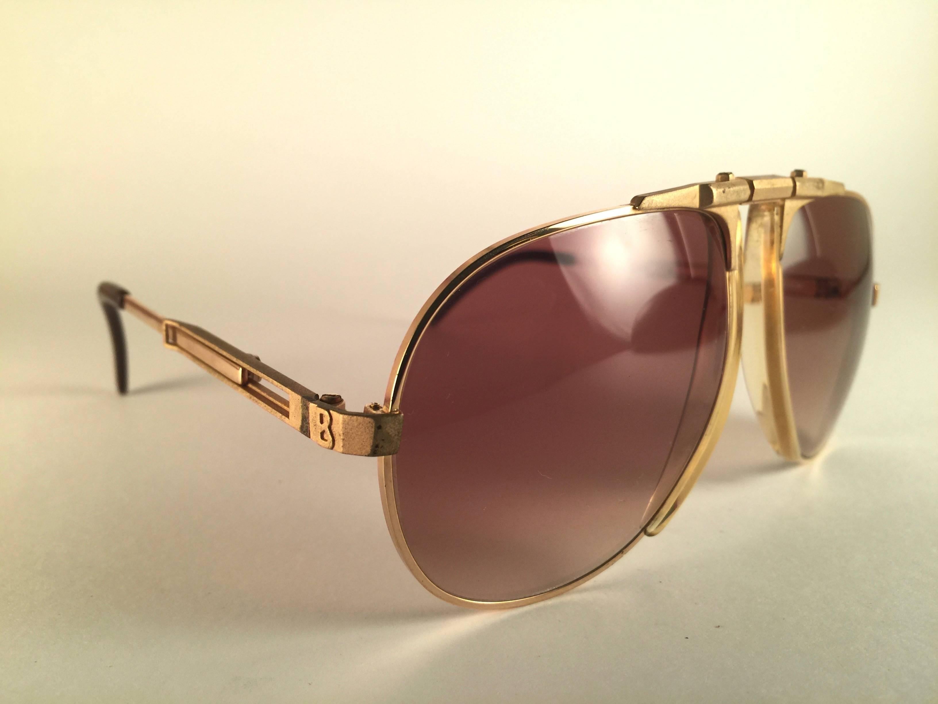 Oggetto raro.   
Occhiali da sole MINT vintage Bogner by Eschenbach 7004 in oro opaco con lenti sfumate marroni. 
Questo paio presenta lievi segni di usura sulle lenti.

La custodia illustrata non è inclusa.
Prodotto in Austria.
