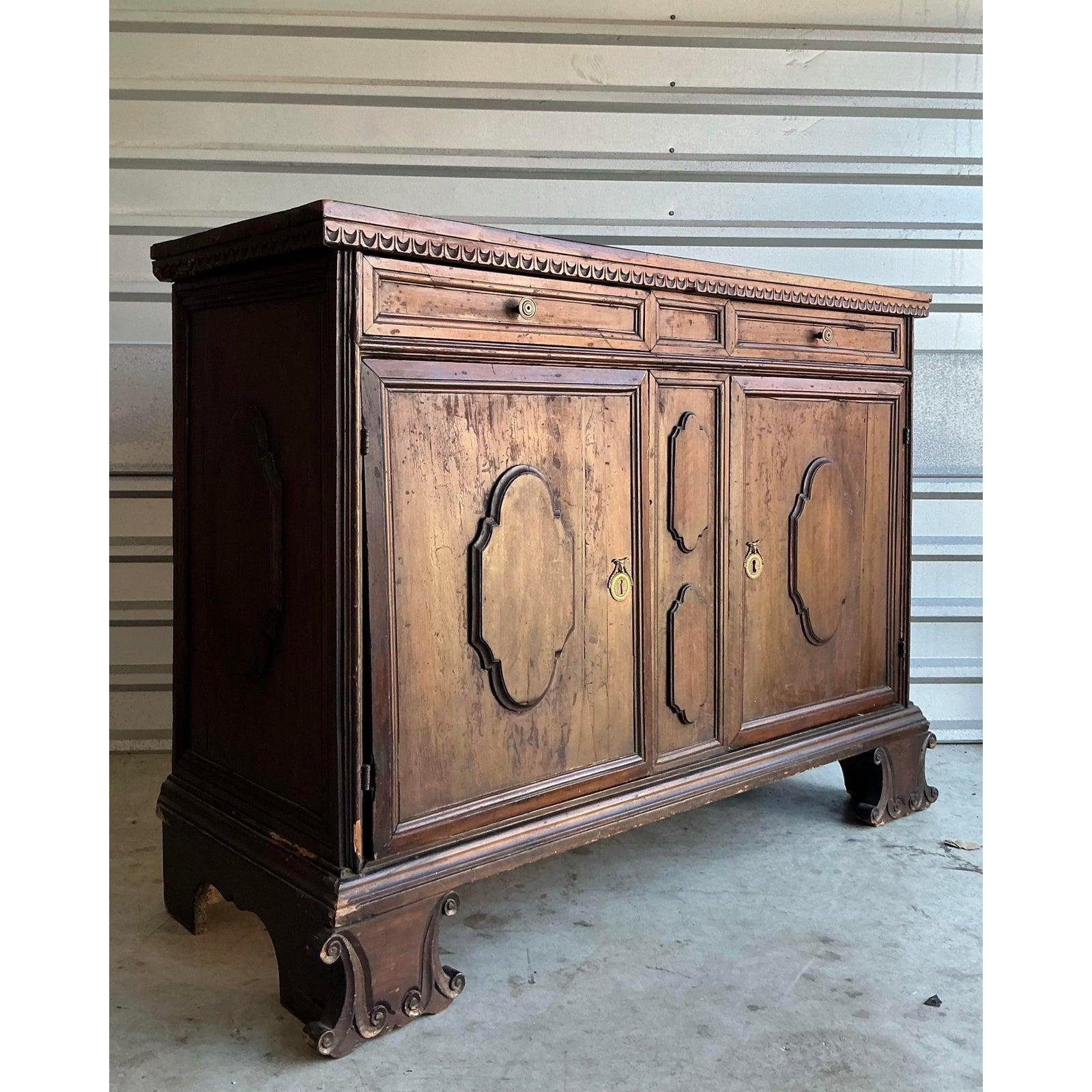 Ti presentiamo un magnifico buffet vintage in noce toscano intagliato, un pezzo sostanzioso che evoca la grandezza e l'eleganza rustica del design europeo del XVIII secolo. Realizzato in noce scuro e ricco, questo buffet presenta squisiti dettagli