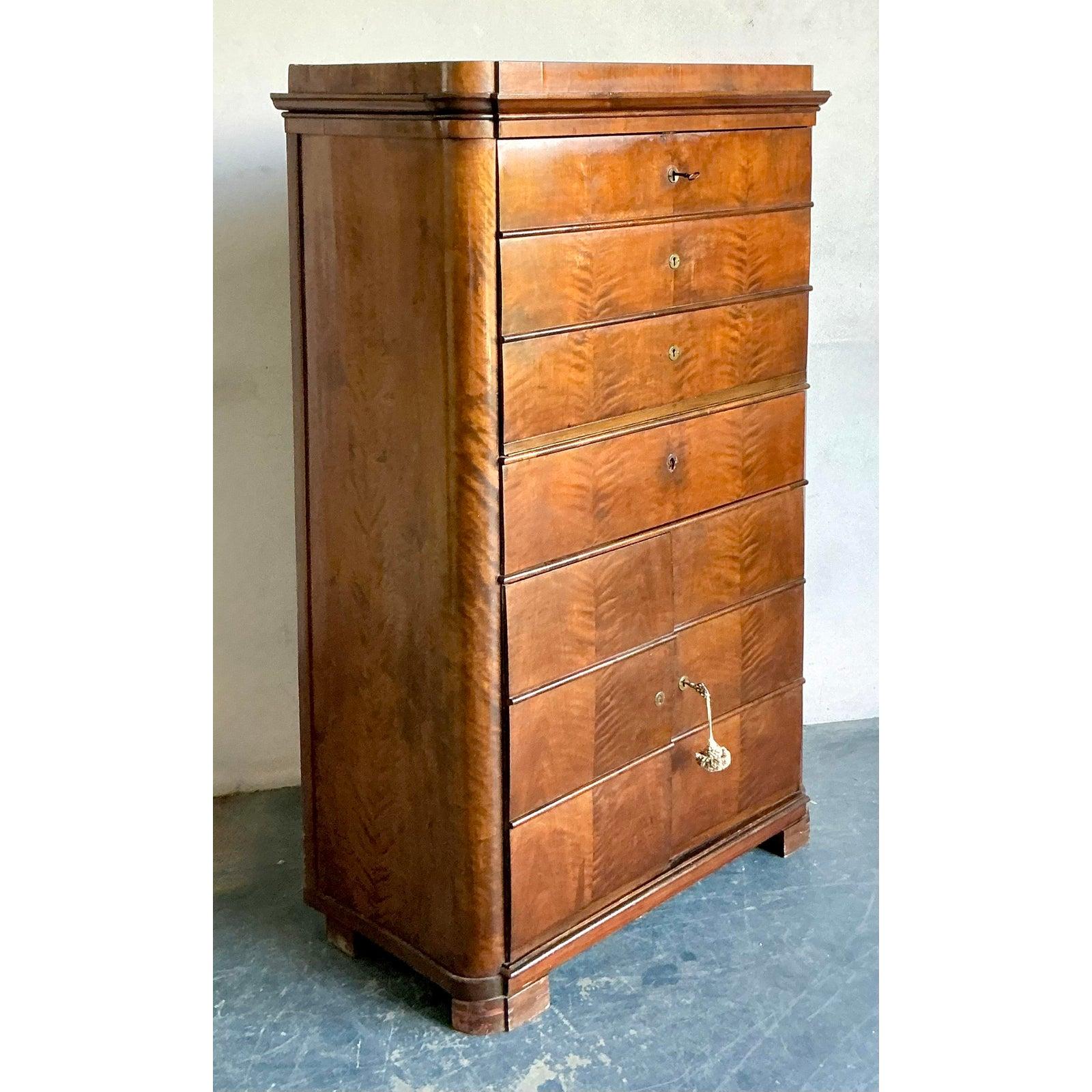 This exceptional antique tall chest embodies the streamlined elegance of the Biedermeier style, which flourished in Central Europe during the early 19th century. Crafted from richly figured walnut or mahogany veneer, the chest features a commanding,