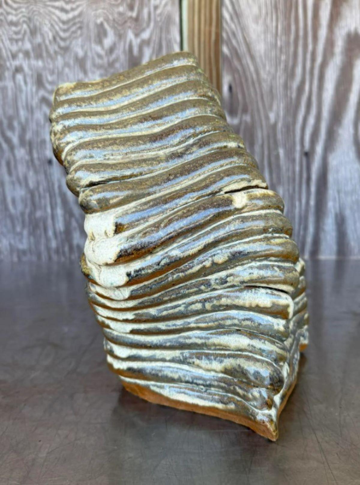 This sculptural piece resembles a highly stylized boot or wedge heel, with an exaggerated, organic form that spirals upward in layered ridges. Its surface is richly textured with horizontal, wave-like grooves that give the impression of sedimentary