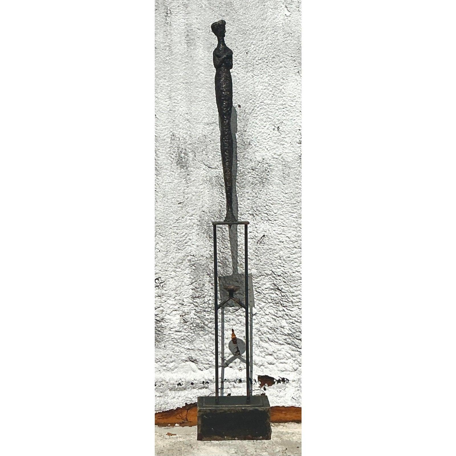 Trasmetti lo spirito potente ed esistenziale di Alberto Giacometti con questa magnifica scultura vintage da pavimento. Questo pezzo monumentale presenta una figura femminile allungata e altamente stilizzata, resa in un metallo patinato e fortemente