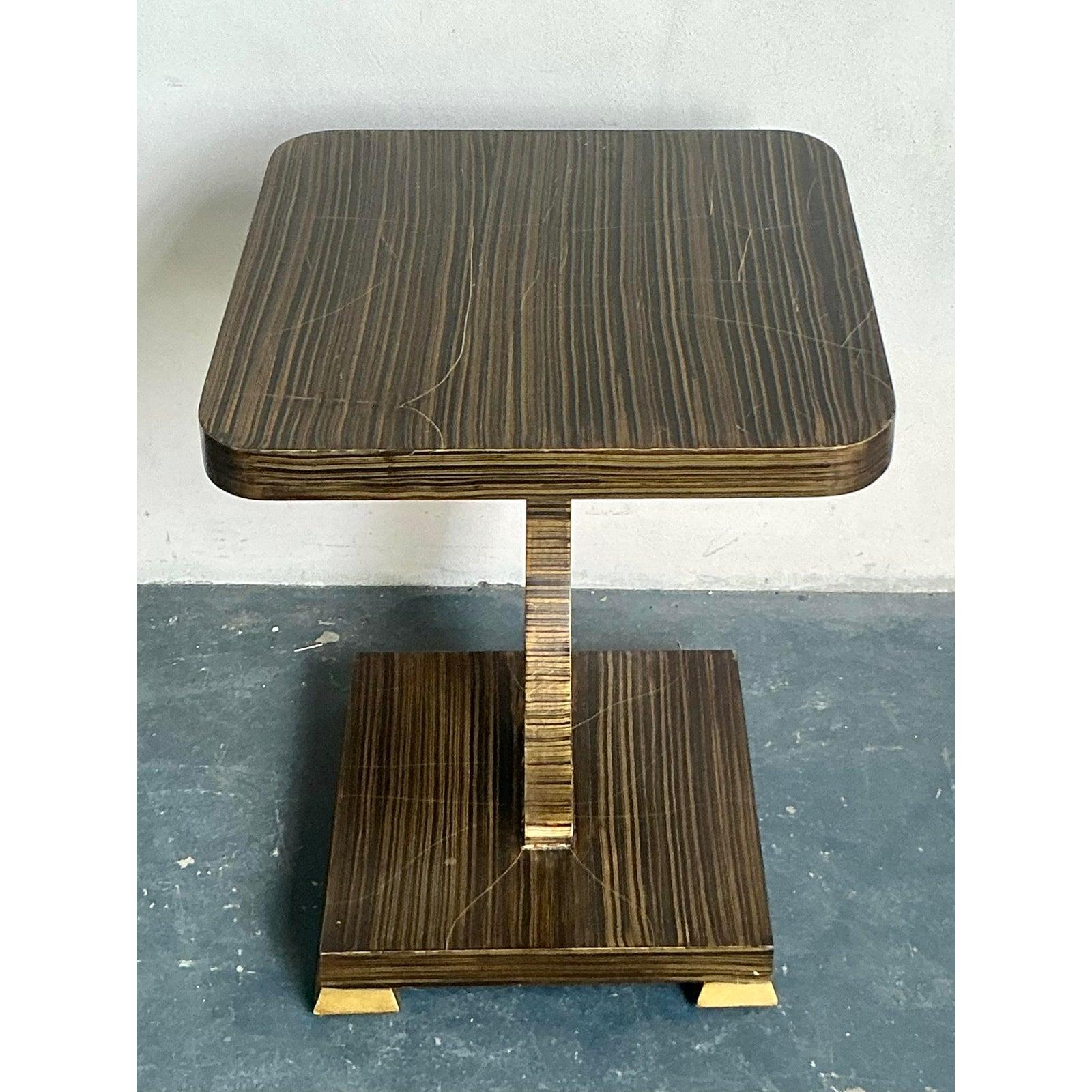 Descubre el sofisticado encanto de esta Mesa auxiliar con punta dorada Amy Howard Vintage Boho, una pieza única que fusiona con elegancia el espíritu bohemio con las líneas de inspiración Art Déco. La mesa presenta un llamativo acabado de imitación