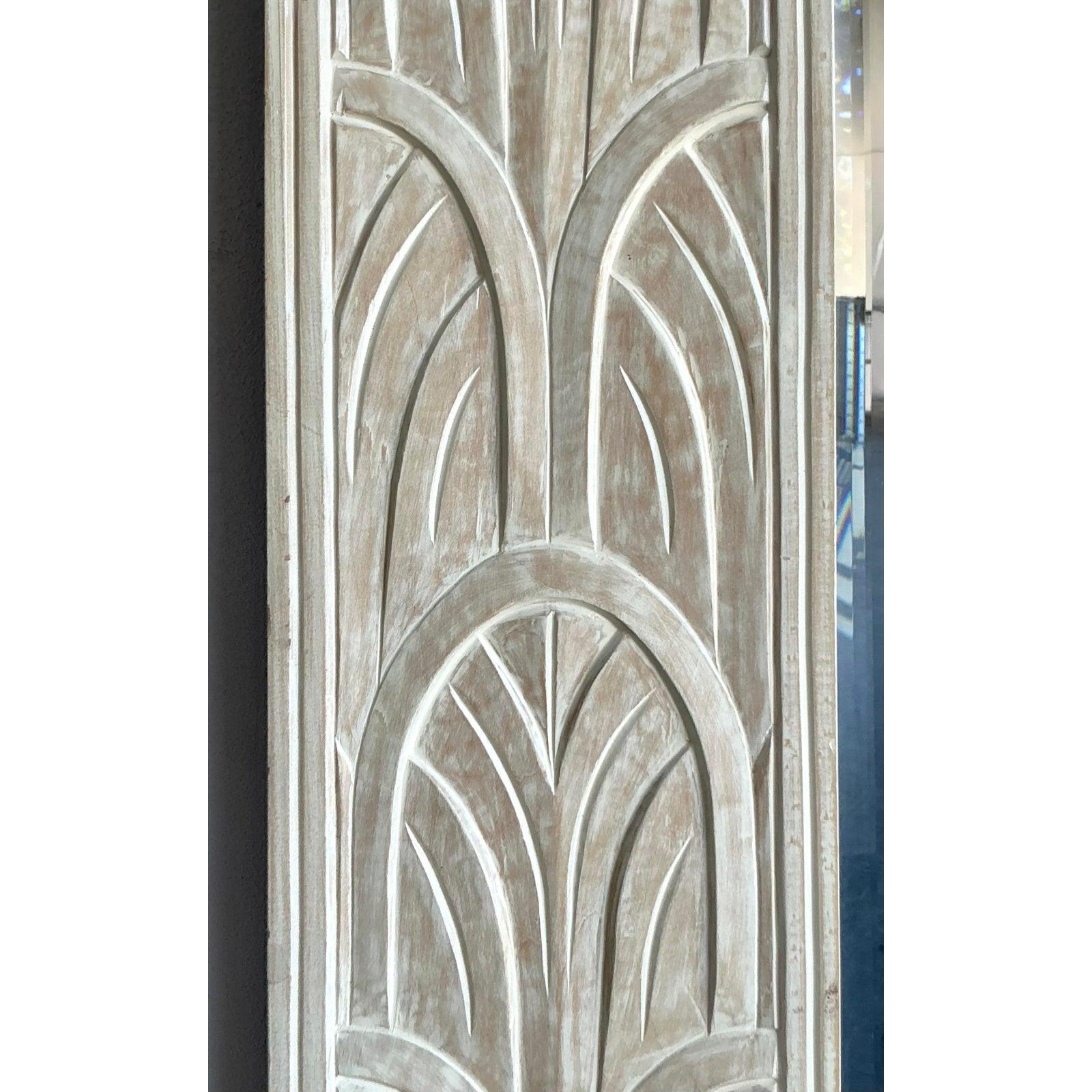 Este llamativo espejo rectangular está enmarcado por un impresionante borde profundamente tallado con motivos repetidos de abanicos y festones Art Decó, que reflejan la elegante geometría de los años 20 reinterpretada para la era posmoderna. El