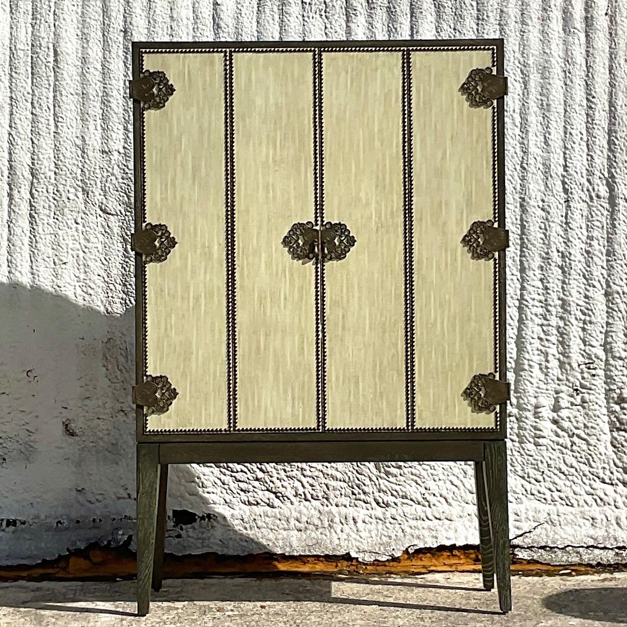 A spectacular vintage Boho dry bar cabinet. The iconic Arteriors 60 inch Chelsey cabinet. Beautiful wrapped linen doors with nailhead trim and engraved hardware. Chic mirrored interior with glass helped. A cerused charcoal finish. Acquired from a