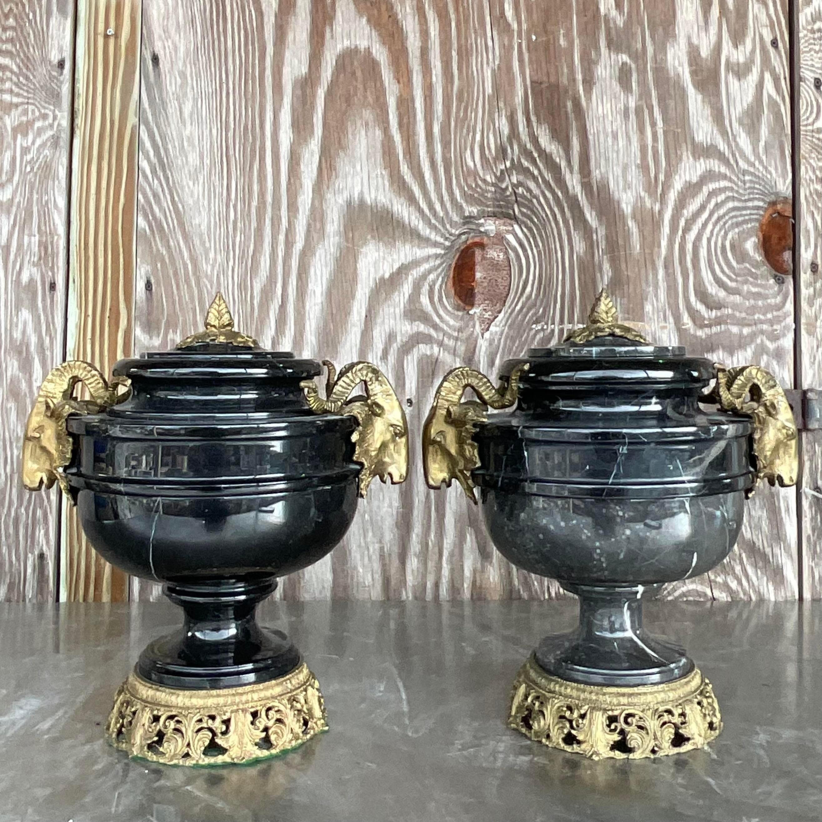 Elevate your decor with this striking pair of vintage urns featuring black marble and brass ram's head motifs. Combining bohemian flair with timeless elegance, these pieces add a touch of sophistication to any American-style interior, exuding a