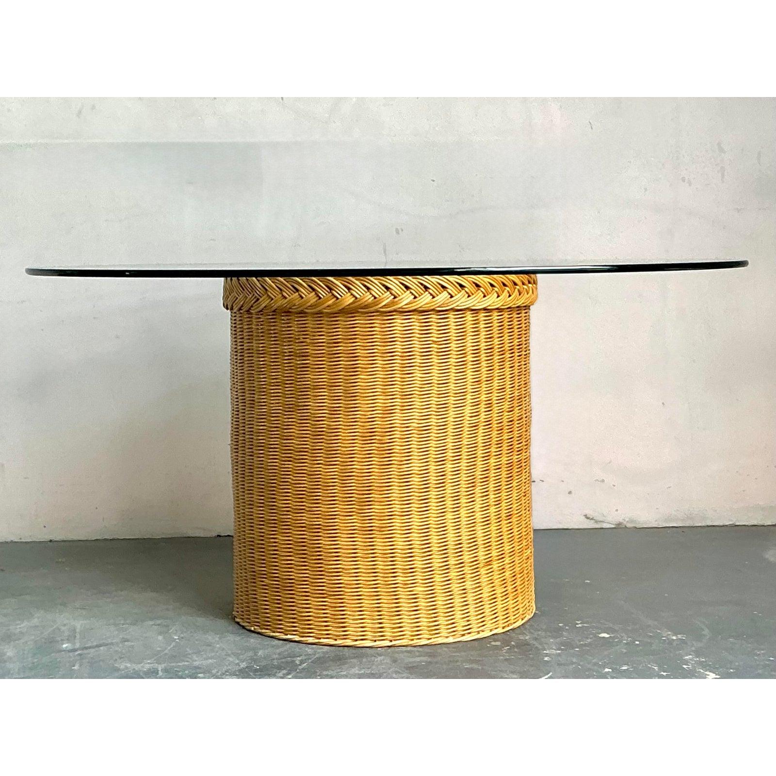 This elegant vintage dining table perfectly captures the refined yet relaxed aesthetic of Coastal and Tropical design popular in the 1980s. The striking cylindrical pedestal base is meticulously hand-woven in natural rattan and wicker, featuring a