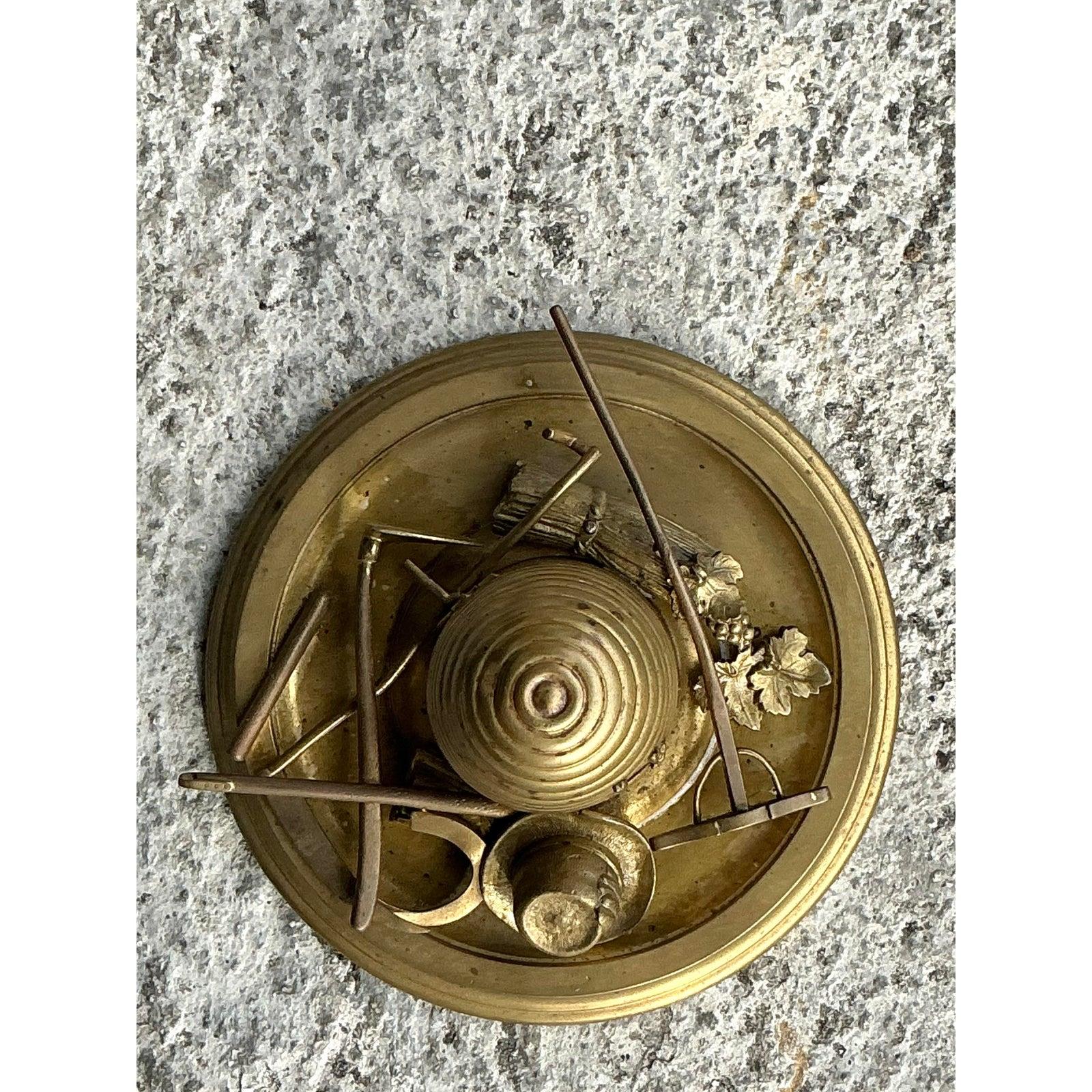 Diese exquisite Vintage-Messing-Honigtopf-Skulptur ist ein einzigartiges Dekorationsstück, das den Charme der rustikalen Imkerei mit bemerkenswerter Kunstfertigkeit einfängt. Der fein gearbeitete Bienenstock sitzt auf einem runden Sockel, der mit