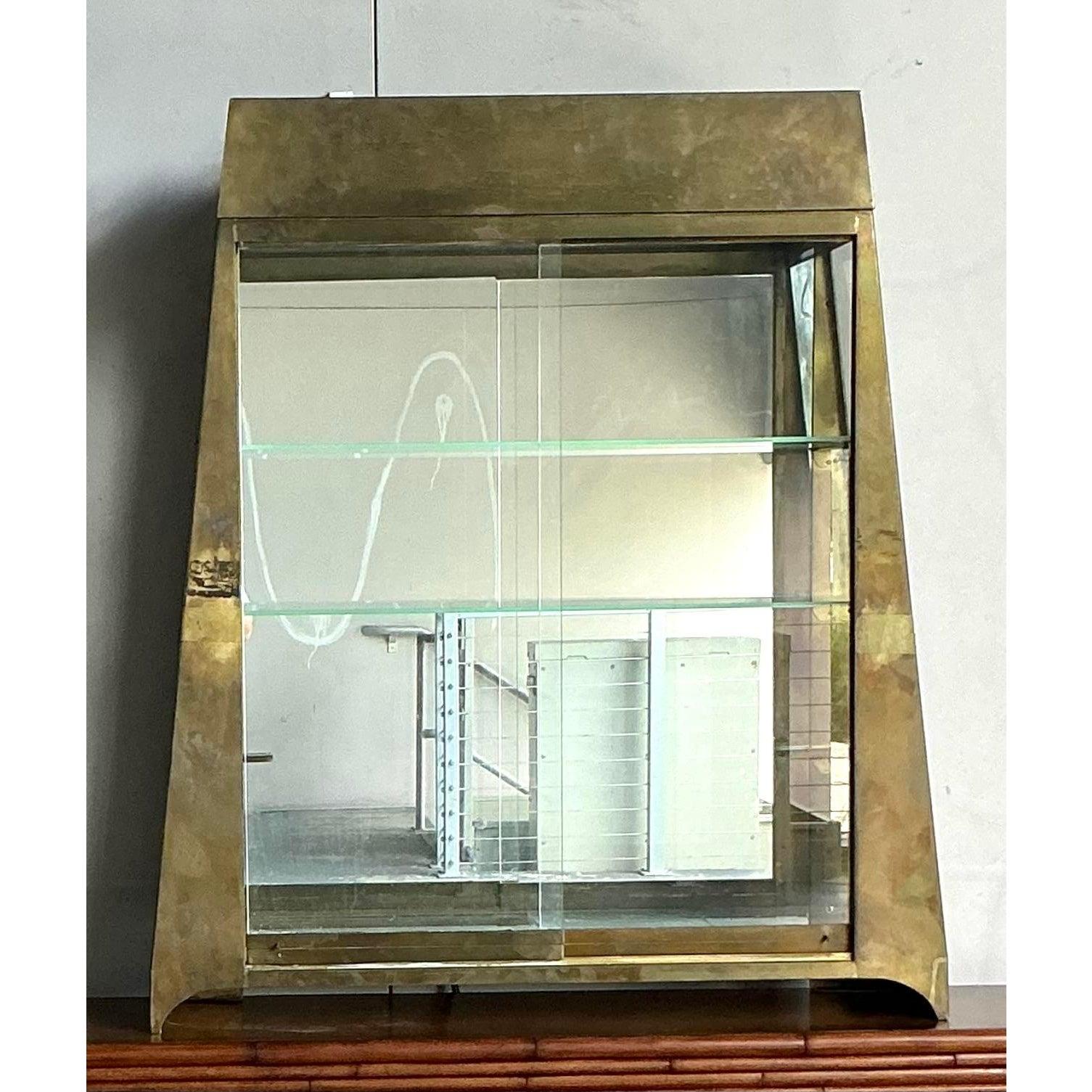 Scopri la versatilità chic di questa splendida étagère in ottone vintage. Definito dalla sua audace forma architettonica e dalla calda finitura in ottone invecchiato, questo pezzo è una masterclass in esposizione sofisticata. Lo schienale a specchio