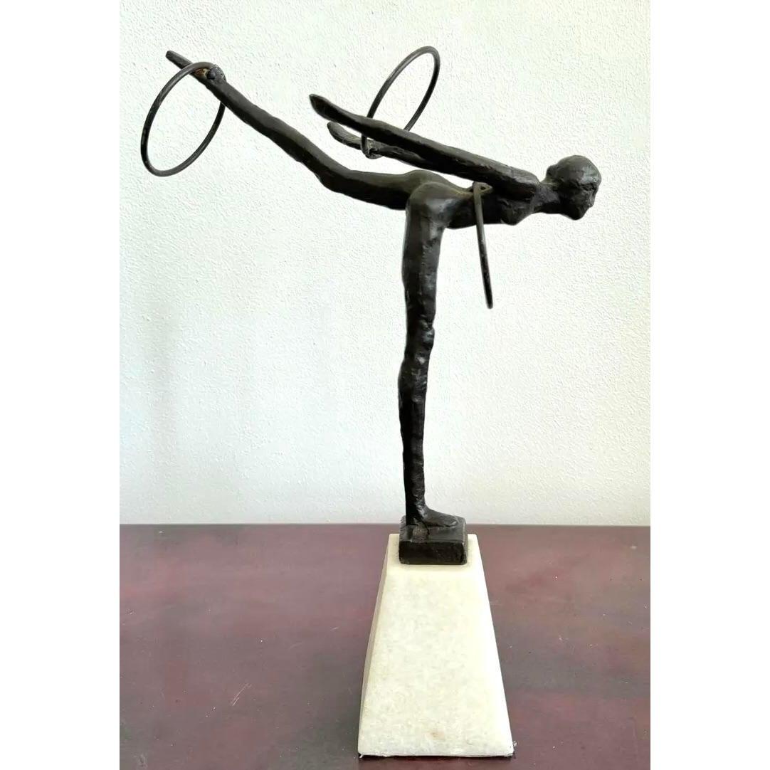 Questa sottile scultura in bronzo cattura un momento di perfetta tensione e grazia, bilanciando la forma umana con l'eleganza astratta. La figura allungata è congelata a metà, piegata in avanti con una gamba estesa all'indietro in un gesto che