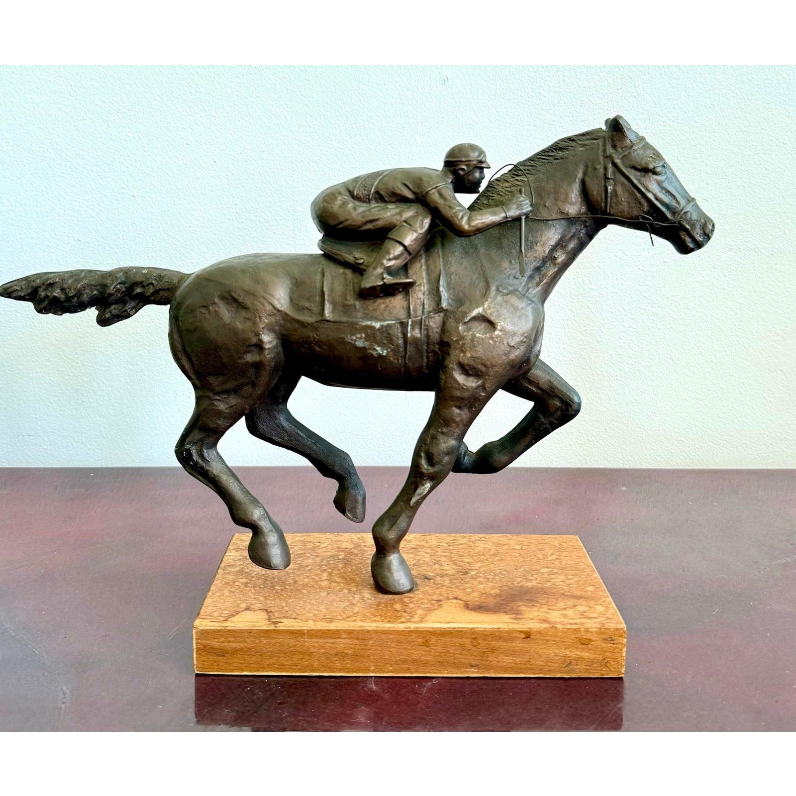 Questa dinamica scultura in bronzo cattura lo slancio di un cavallo da corsa al galoppo, con il suo fantino accucciato in perfetta sincronia. La tensione nella falcata del cavallo e la concentrazione impressa sul volto del cavaliere danno vita alla