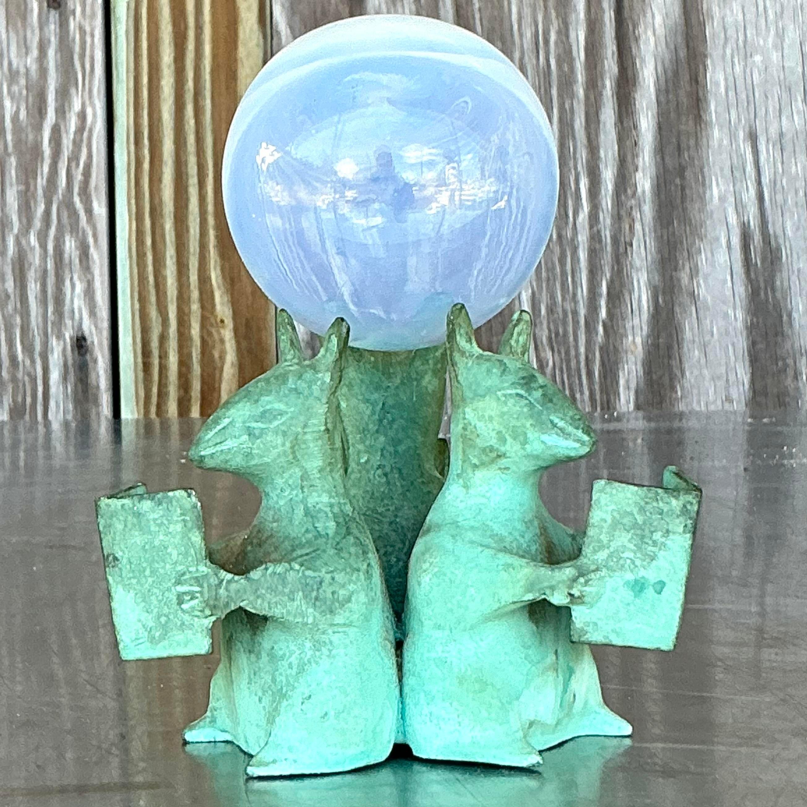 This Vintage Boho Bronze Mice Cradle with Glass Orb exudes whimsical charm and artistic flair, characteristic of American boho style. The intricate bronze mice design cradling a delicate glass orb creates a captivating and unique piece, perfect for
