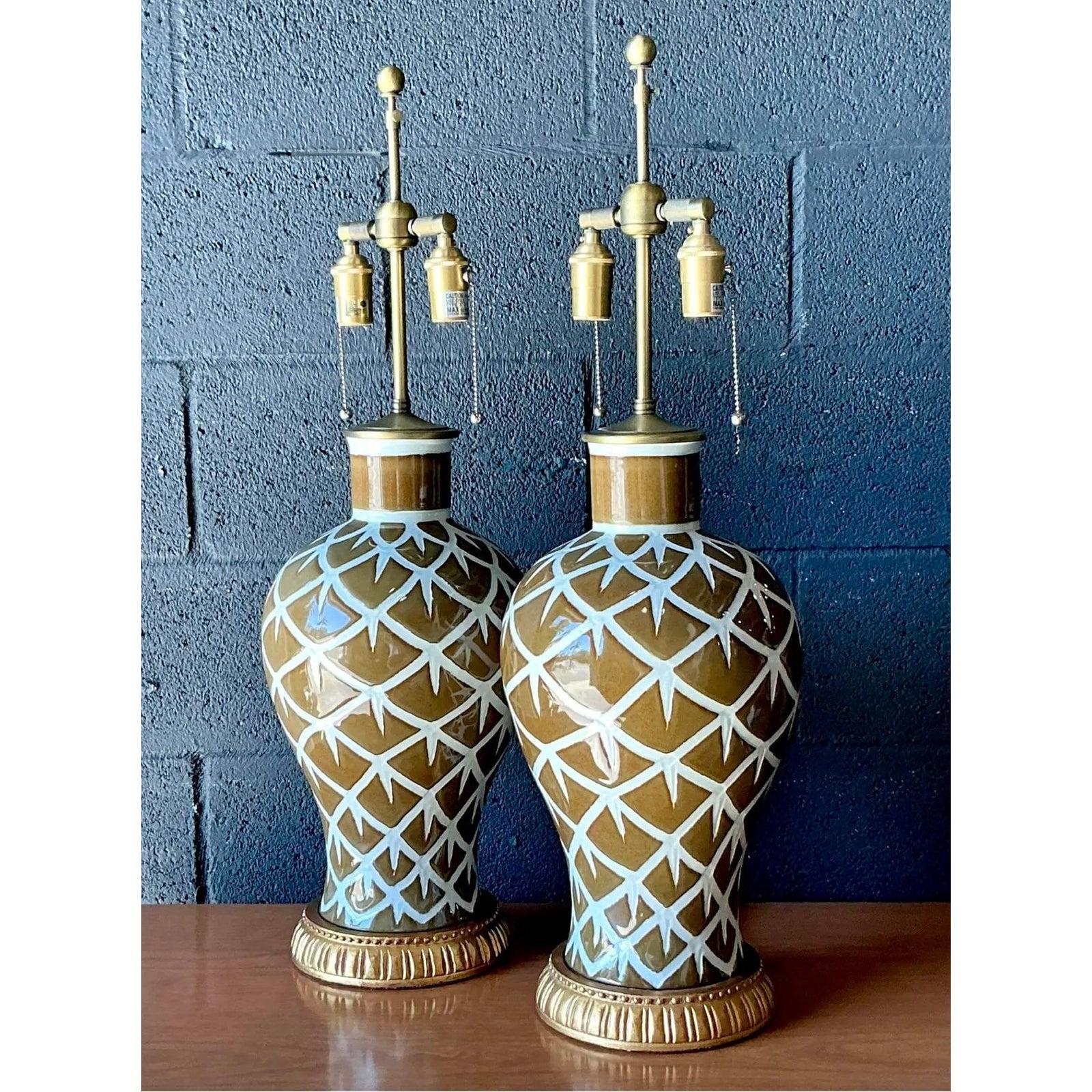 This exceptional pair of vintage table lamps embodies the sophisticated transition between Mid-Century Modern flair and dramatic Hollywood Regency detailing. The substantial ceramic bases feature a classic urn shape adorned with a crisp white glaze