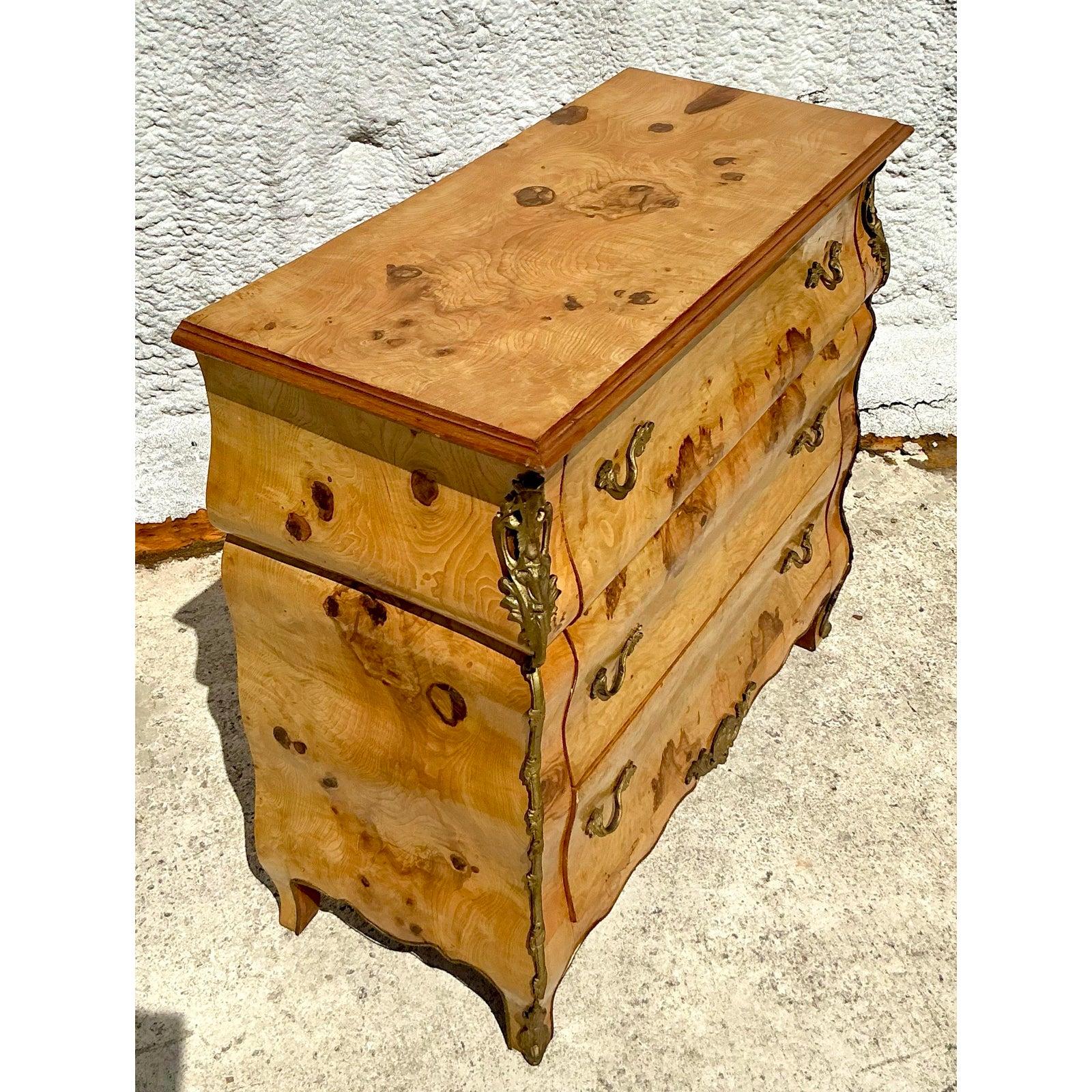 Experience the opulent beauty of this vintage chest of drawers, a piece that effortlessly blends luxurious materials with a classic form. Crafted with exquisite burl wood veneer that showcases stunning natural patterns, this chest features a