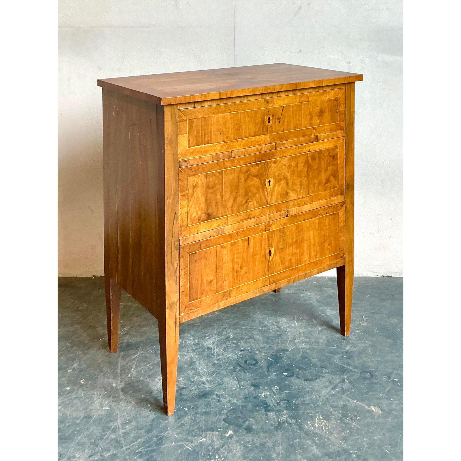 This charming vintage chest of drawers is a superb example of natural elegance and minimalist design. The piece is crafted from beautiful wood, with the drawer fronts and side panels adorned in a stunning burled wood veneer. The unique, swirling