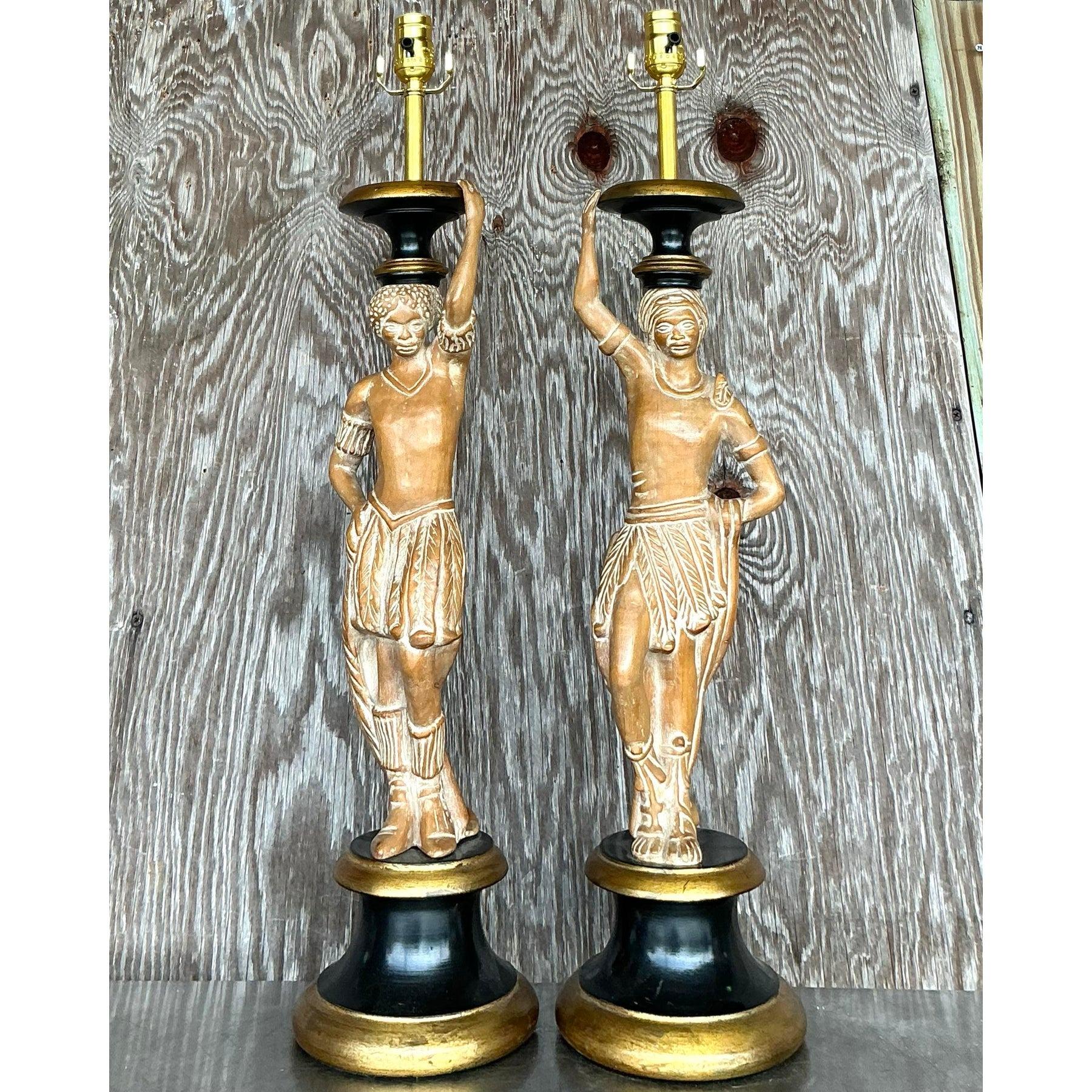 Questa sorprendente coppia di lampade vintage con figure intagliate in stile boho mostra un'eccezionale maestria con dettagli intricati e un fascino scultoreo unico. Le figure in legno intagliato a mano si ergono su eleganti piedistalli neri e