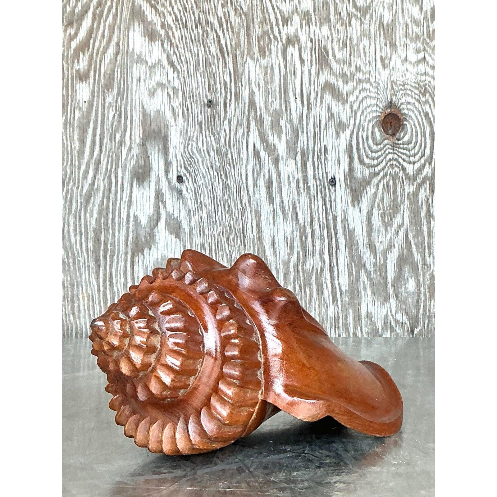 Infuse your space with organic coastal elegance through this stunning vintage hand-carved wooden conch shell sculpture. Carefully sculpted from solid wood, this piece showcases exquisite craftsmanship with its graceful curves and deeply carved