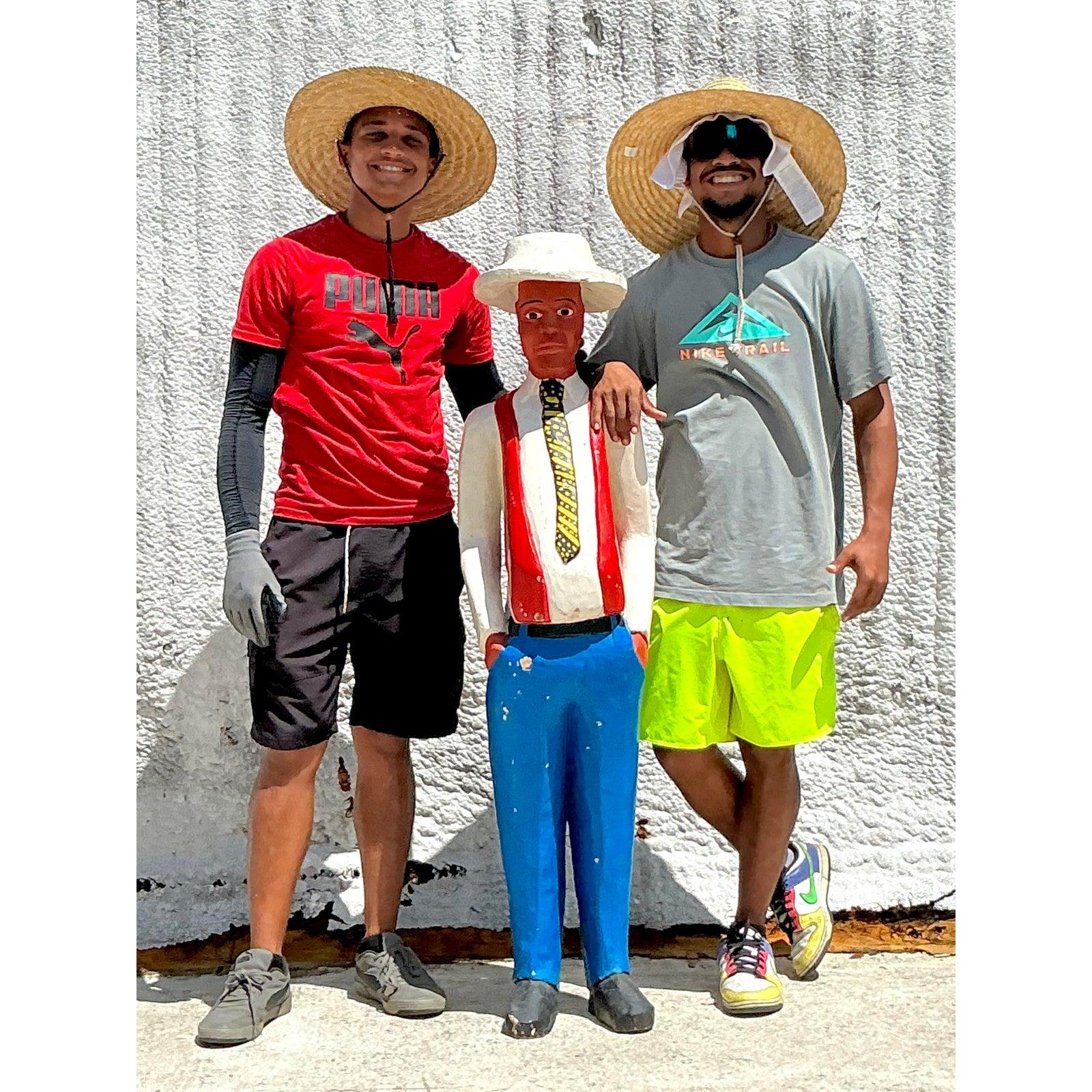 Questa scultura di uomo cubano in legno intagliato in stile boho vintage conferisce una personalità stravagante e un fascino culturale a qualsiasi spazio. Alta più di un metro e mezzo, questa figura intagliata e dipinta a mano presenta vivaci colori
