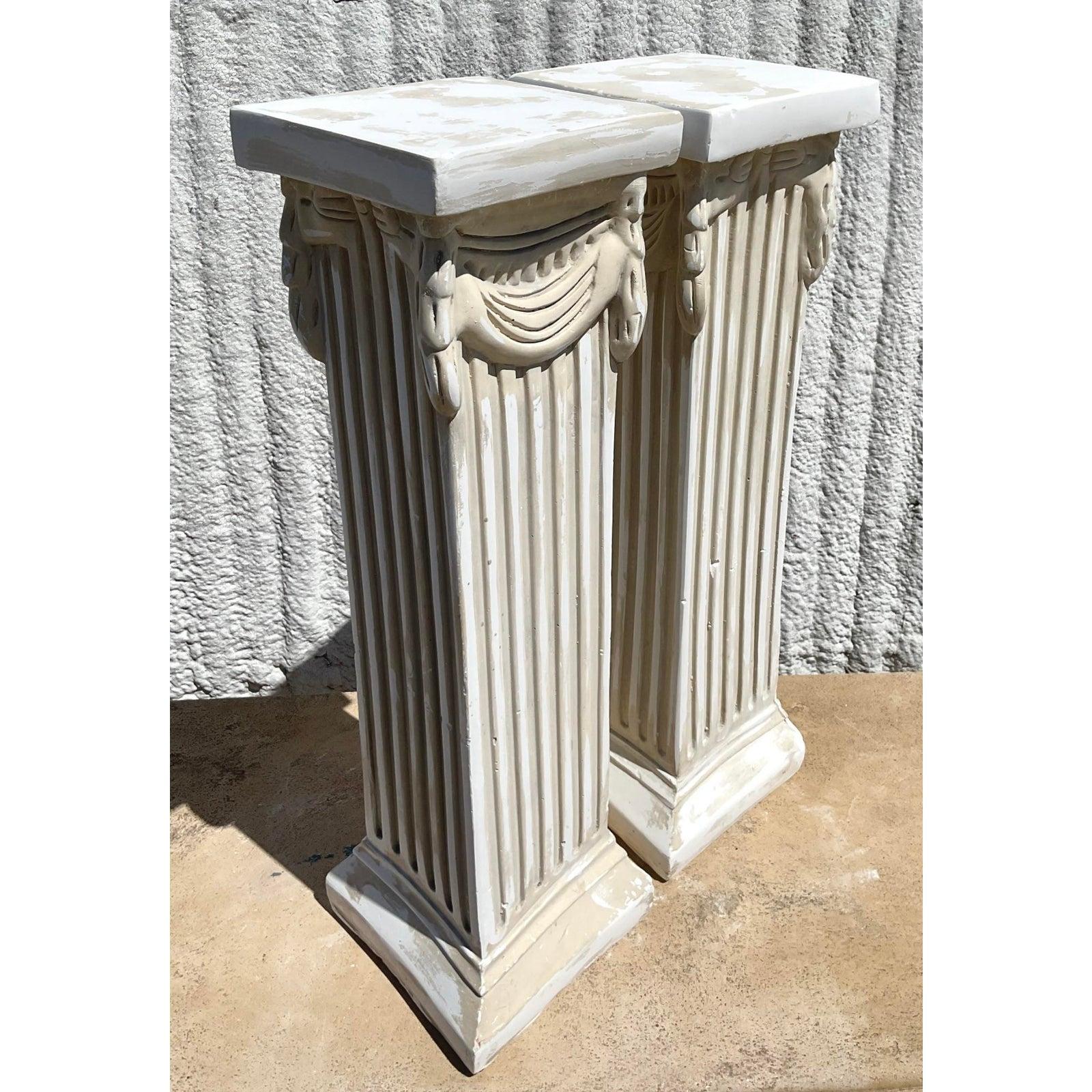 Élevez votre espace avec cette paire exquise de piédestaux-colonnes vintage en plâtre moulé sur bois, riche en style néoclassique. Chaque piédestal présente des fûts finement cannelés et des guirlandes ornées inspirées de l'ancien design