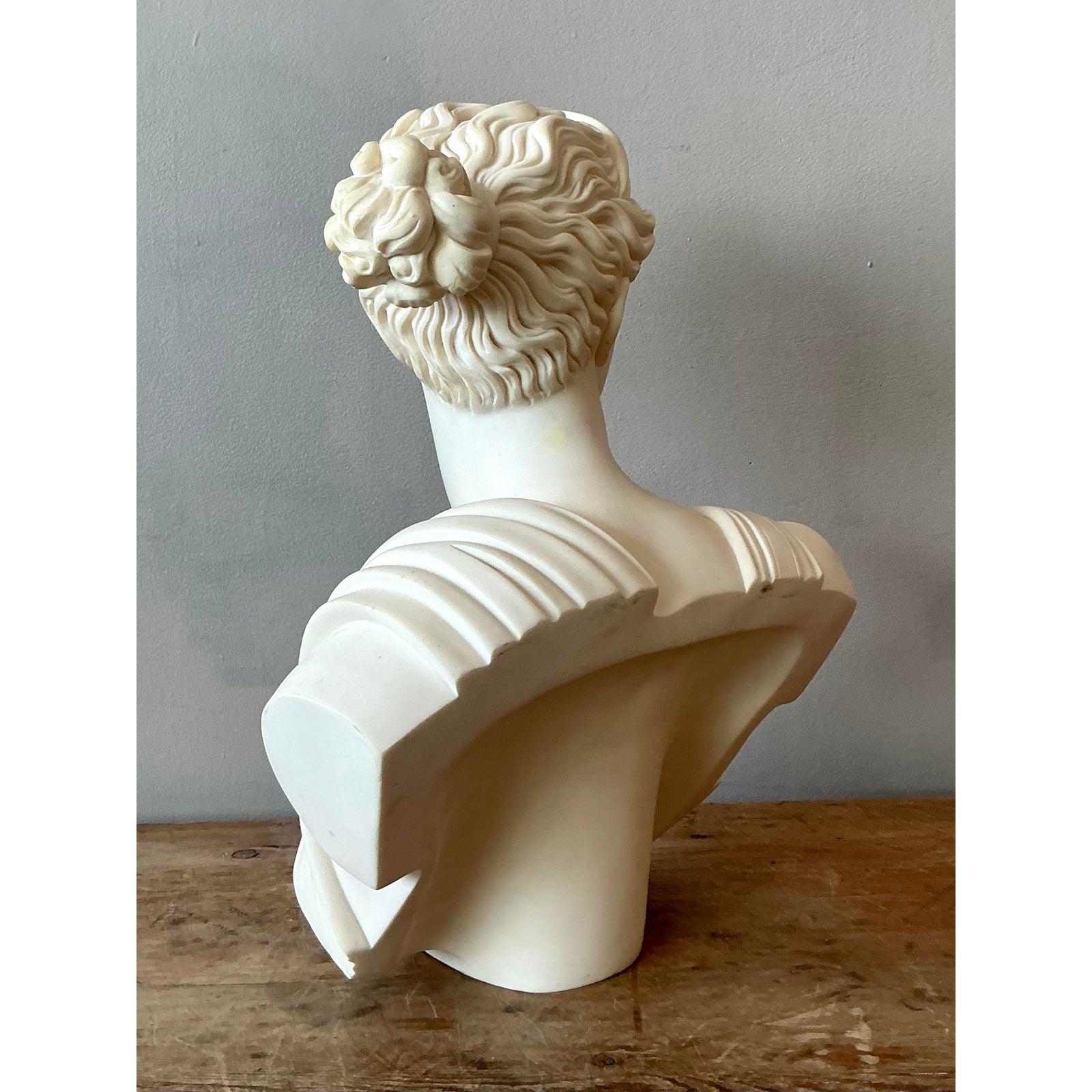 Un imponente busto d'epoca in pietra fusa che raffigura con eleganza Artemis, la dea greca della caccia, della natura selvaggia e della luna, spesso identificata con la Diana romana. Questa squisita scultura cattura la bellezza classica e la forza