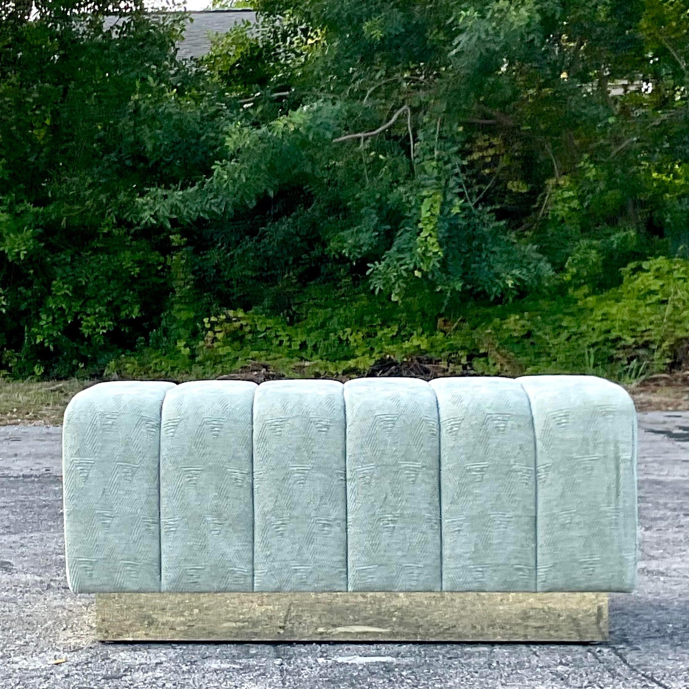 A striking vintage Boho ottoman. A chic channel tufted piece with a wrap around laminated brass plinth. Custom built and solid. Acquired from a Palm Beach estate.