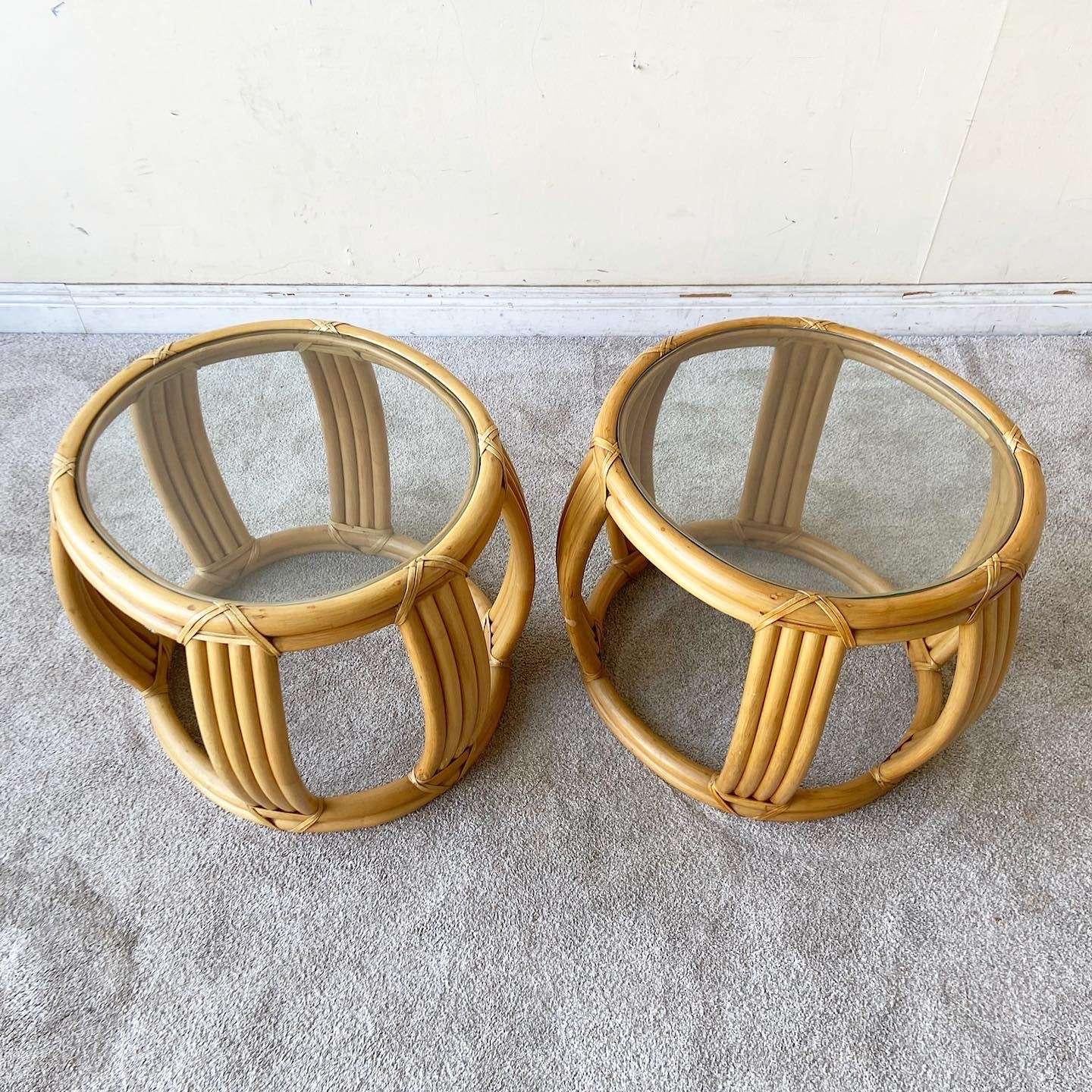 Exceptional pair of vintage bohemian bamboo rattan side tables. Features an oval shape with a glass top.l and natural finish.